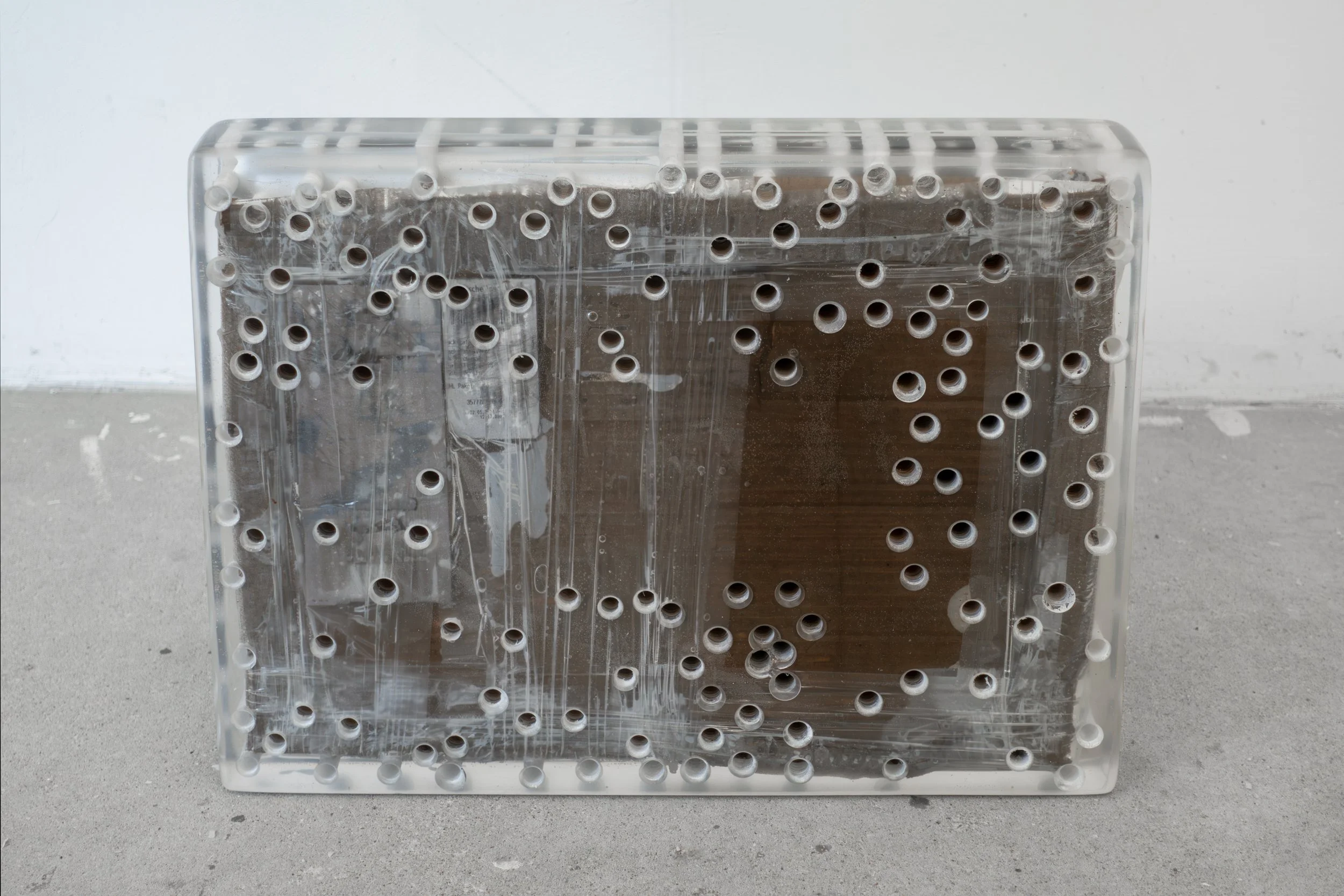  JASON GRINGLER.  EBAY SCULPTURE (PACKAGE) (2024).  STUDIO VIEW.  LAPTOPS, PACKING TAPE, CARDBOARD, HOLES, WOOD, SILICONE, DETRITUS, EPOXY RESIN.  48 X 35 X 6 CM (19 X 14 X 2 1/2 IN) UNIQUE. 