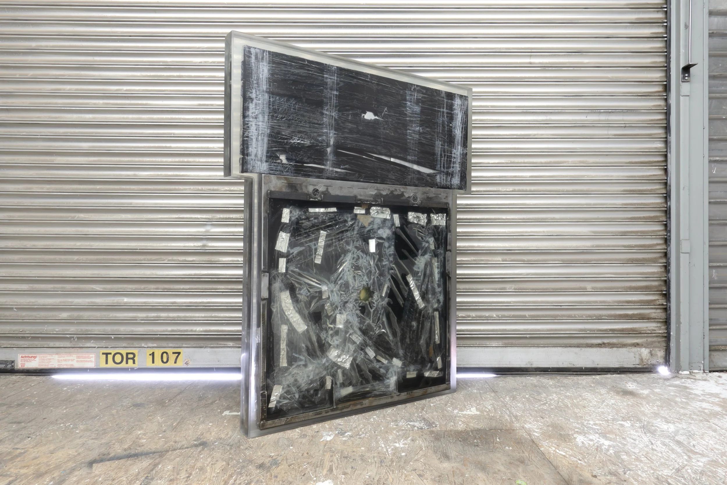  JASON GRINGLER.  TOMB (2026).  STUDIO VIEW.  FAILED ARTWORK, STEEL, PLASTIC WRAP, ALUMINUM TAPE, PACKING TAPE, PIGMENT, WOOD, OBSOLETE TECH, RUST, EPOXY, WAX AND ADHESIVES.  8.5 X 106.5 X 134 CM. 