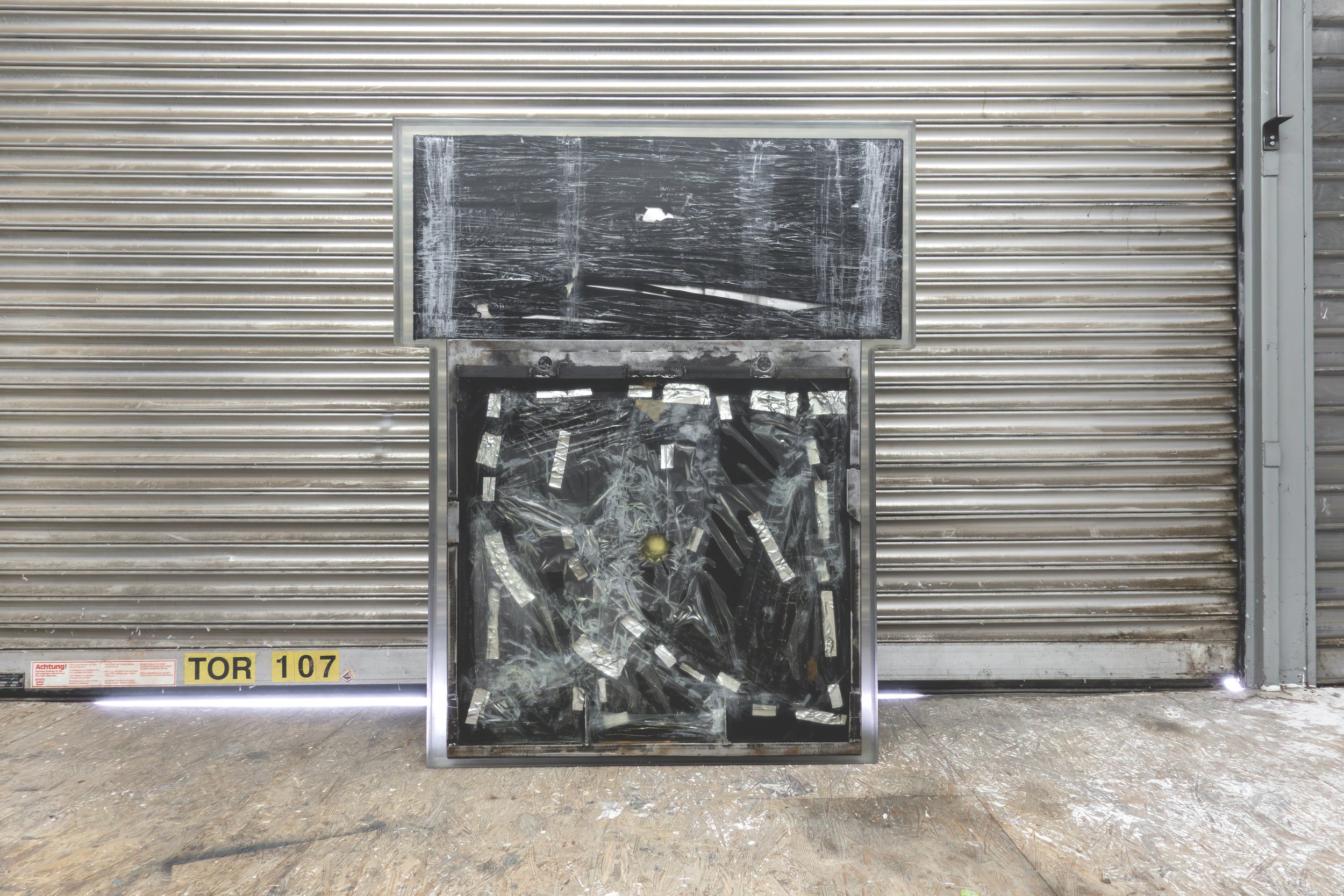  JASON GRINGLER.  TOMB (2026).  STUDIO VIEW.  FAILED ARTWORK, STEEL, PLASTIC WRAP, ALUMINUM TAPE, PACKING TAPE, PIGMENT, WOOD, OBSOLETE TECH, RUST, EPOXY, WAX AND ADHESIVES.  8.5 X 106.5 X 134 CM. 