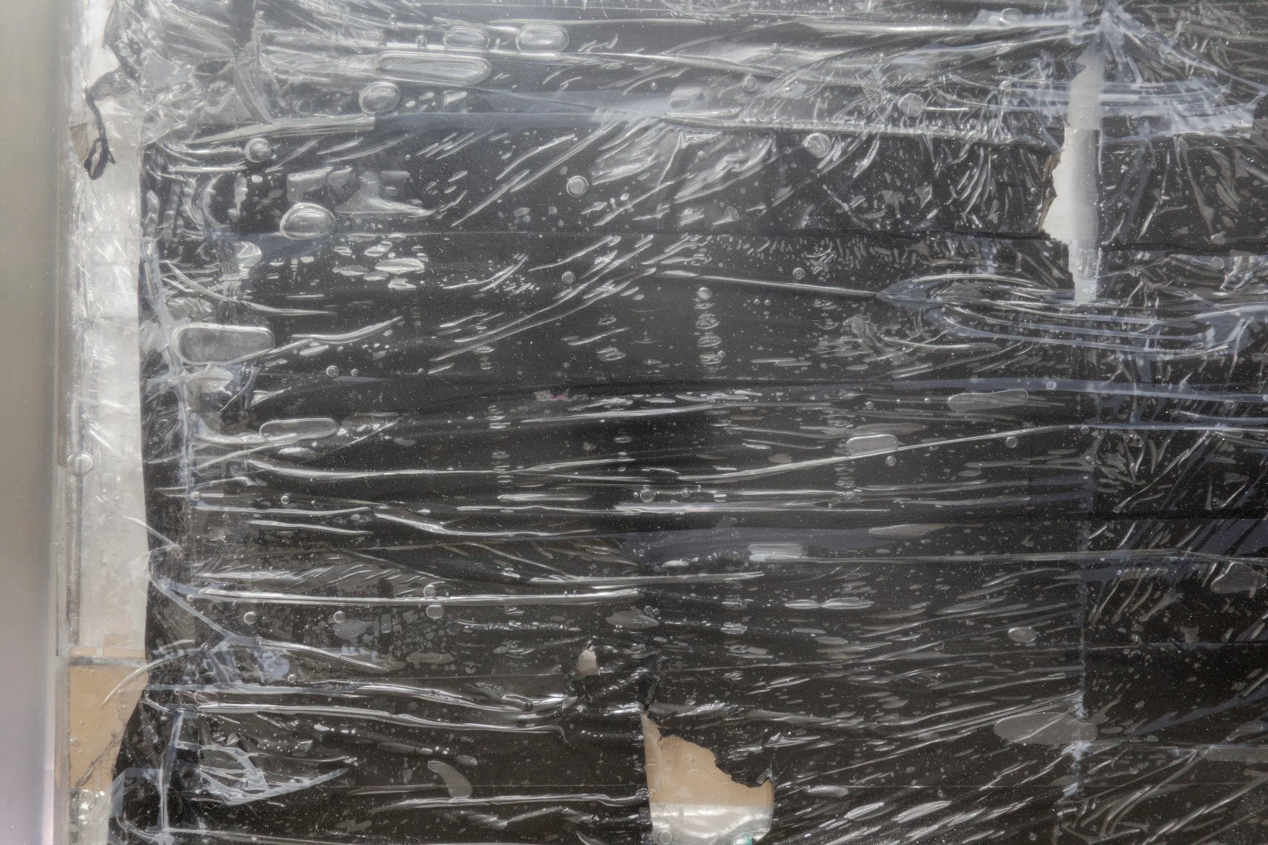  JASON GRINGLER.  TOMB (2026) (DETAIL).  STUDIO VIEW.  FAILED ARTWORK, STEEL, PLASTIC WRAP, ALUMINUM TAPE, PACKING TAPE, PIGMENT, WOOD, OBSOLETE TECH, RUST, EPOXY, WAX AND ADHESIVES.  8.5 X 106.5 X 134 CM. 