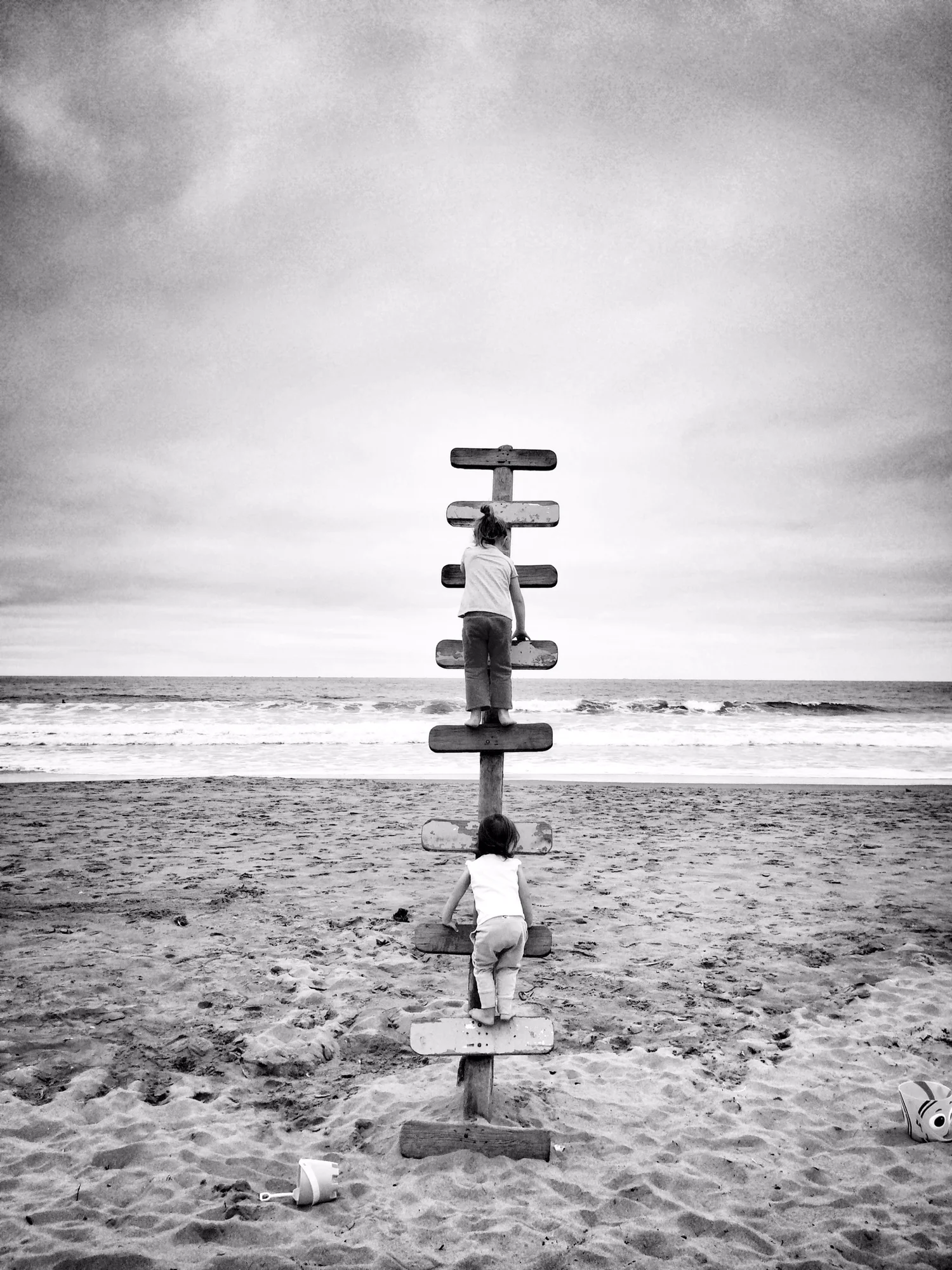 Two children climbing beside the sea, in black and white.