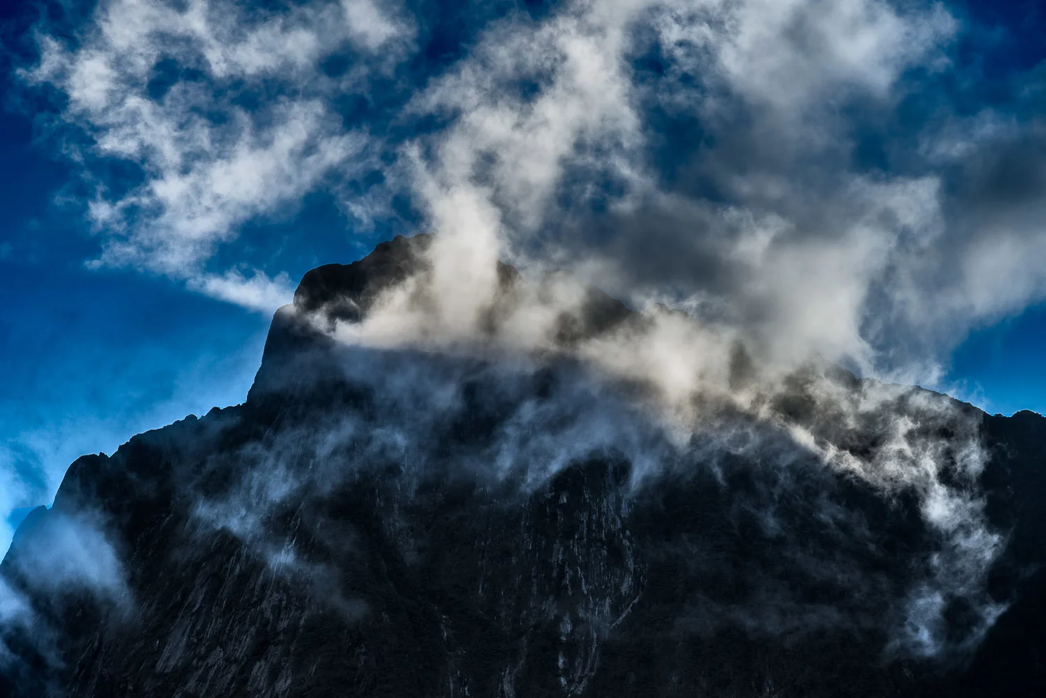 A spectacular scene as light illuminates clouds in front of a mountain top above Milford Sound, New Zealand .