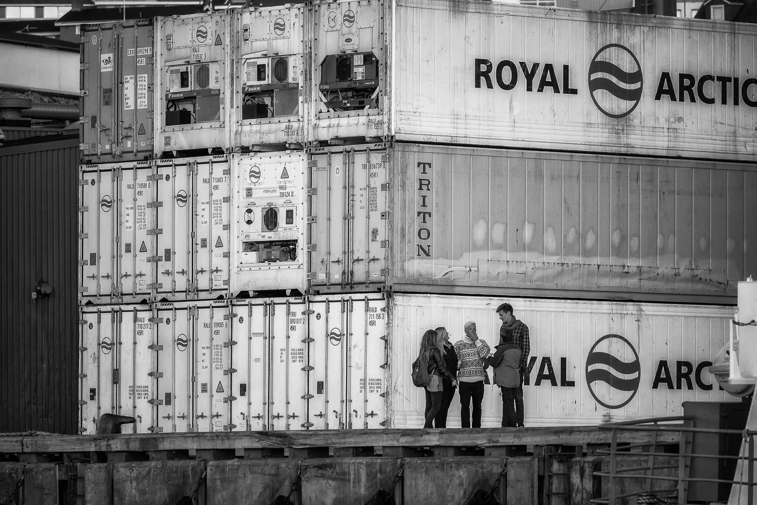 A stack of shipping containers provide an interesting background for a group of tourists on the docks of the harbour at Ilulissat, Greenland.