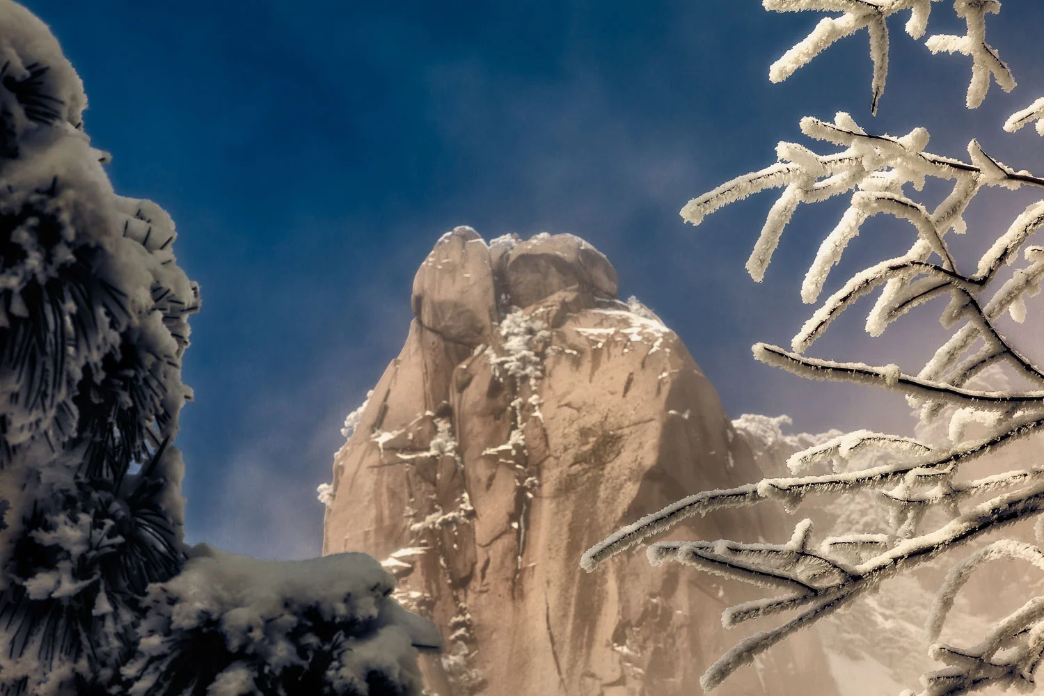A mountain peak, bathed in warm light, is framed by ice encrusted treees on the spectacular Huangshan (i.e., Yellow Mountain) in China .