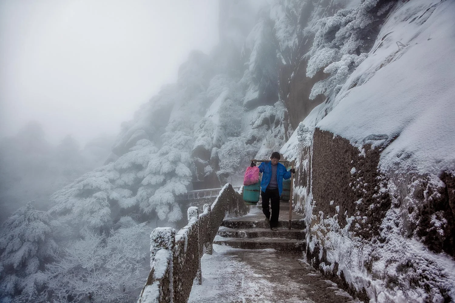 A porter, loaded with goods, walks a windy and exposed path on Huangshan (i.e., Yellow Mountain), China .