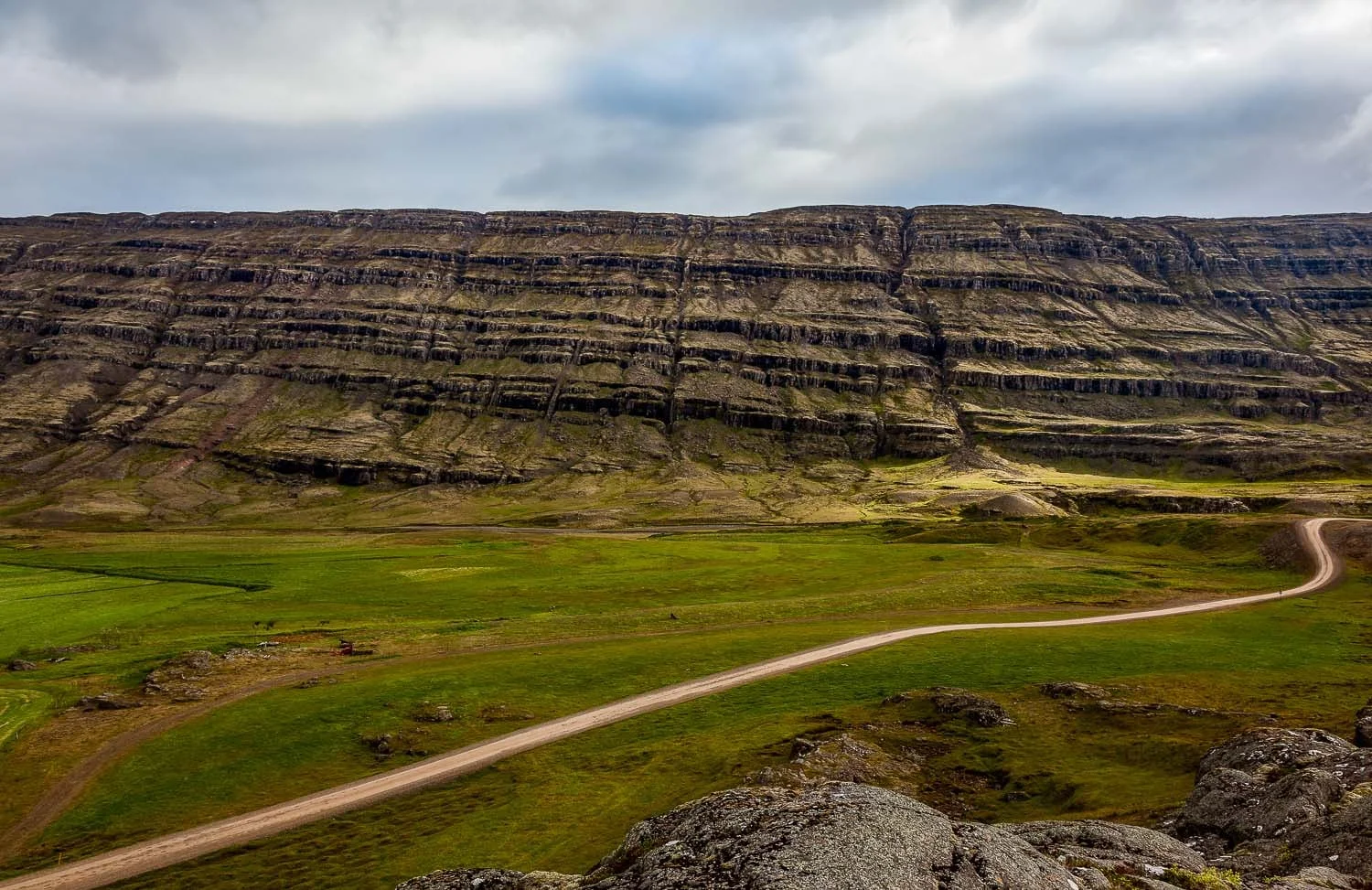 A dry dirt road winds its way through beautiful mountain scenery in rural Iceland .