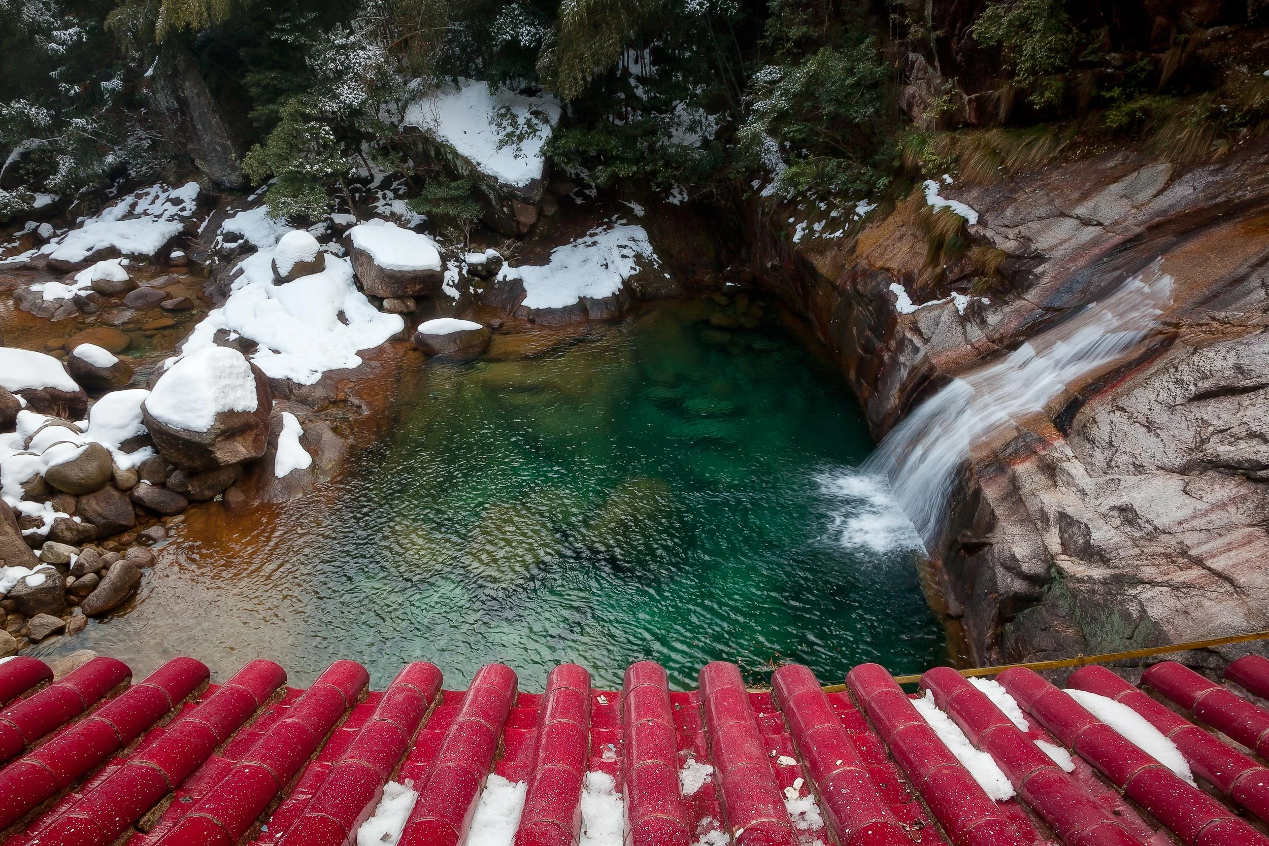 A colorful view, over a pagoda rooftop, down onto a tranquil pool fed by a small waterfall near Huangshan, China .