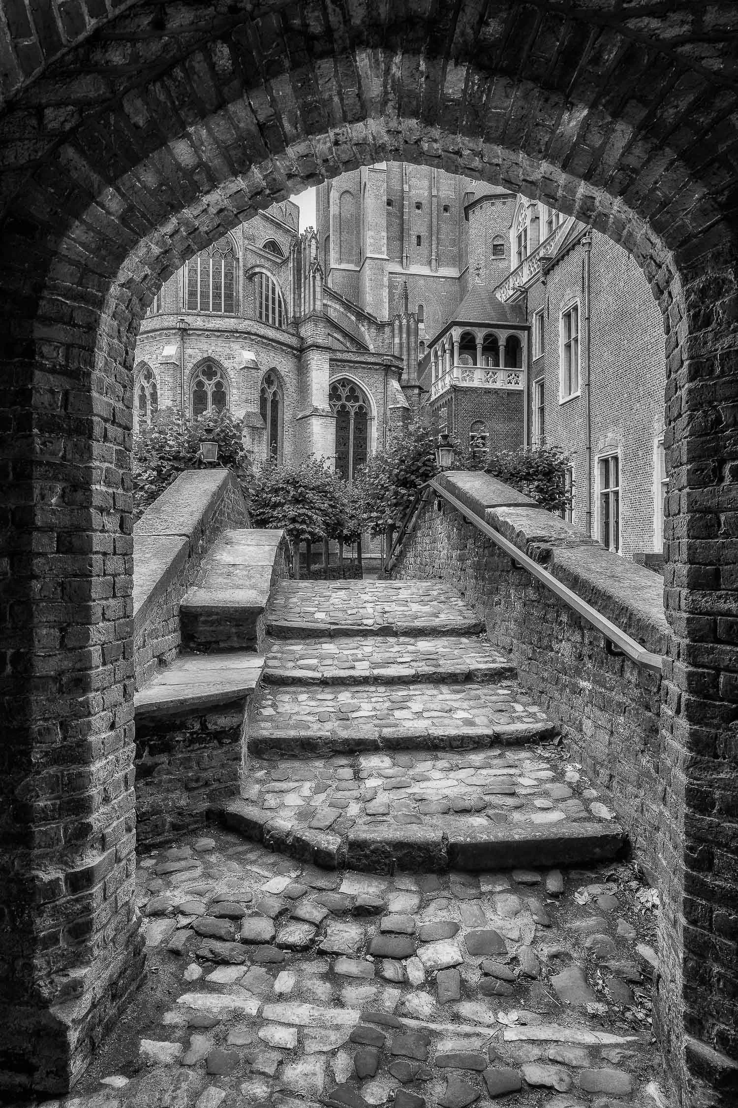 A classic view looking through an archway onto a bridge and onwards towards historic buildings in Bruges, Belgium .