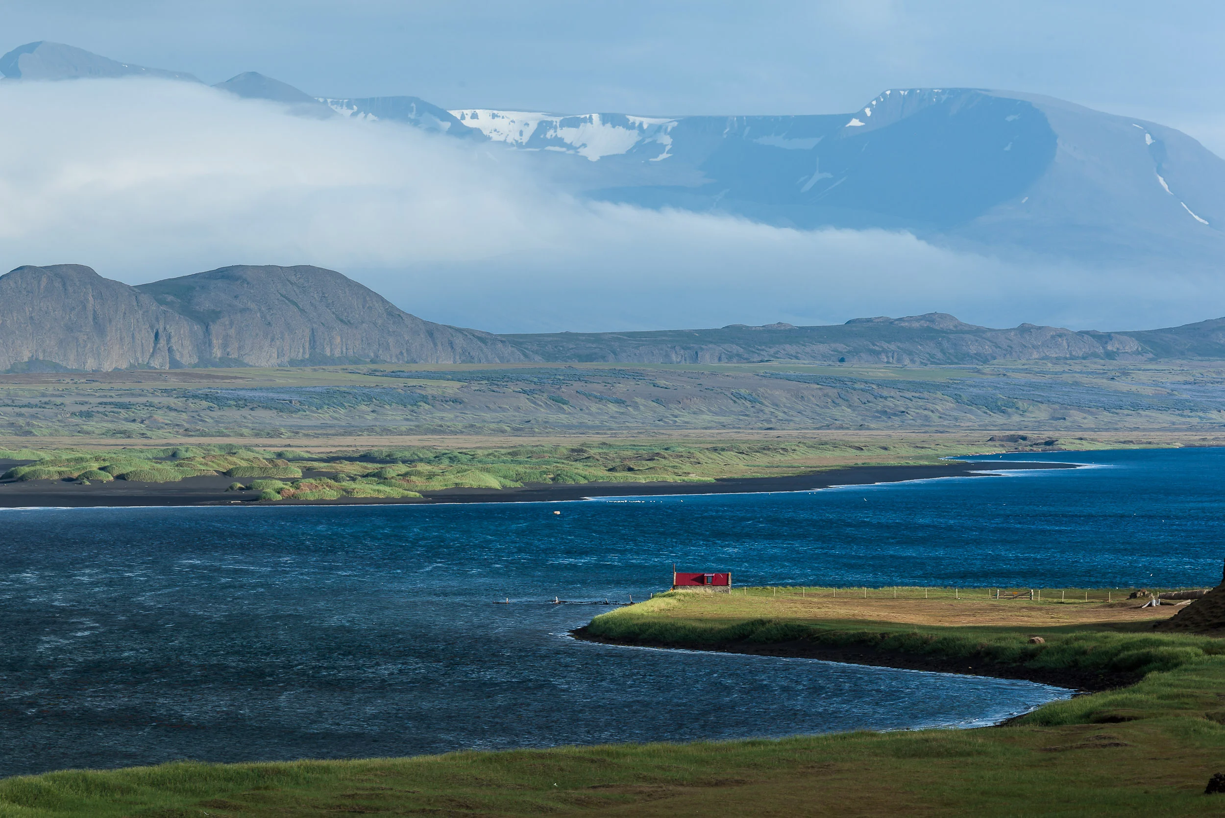 The red roof of a perfectly positioned dwelling, on the edge of a fjord , glows in the sunshine in rural Iceland .