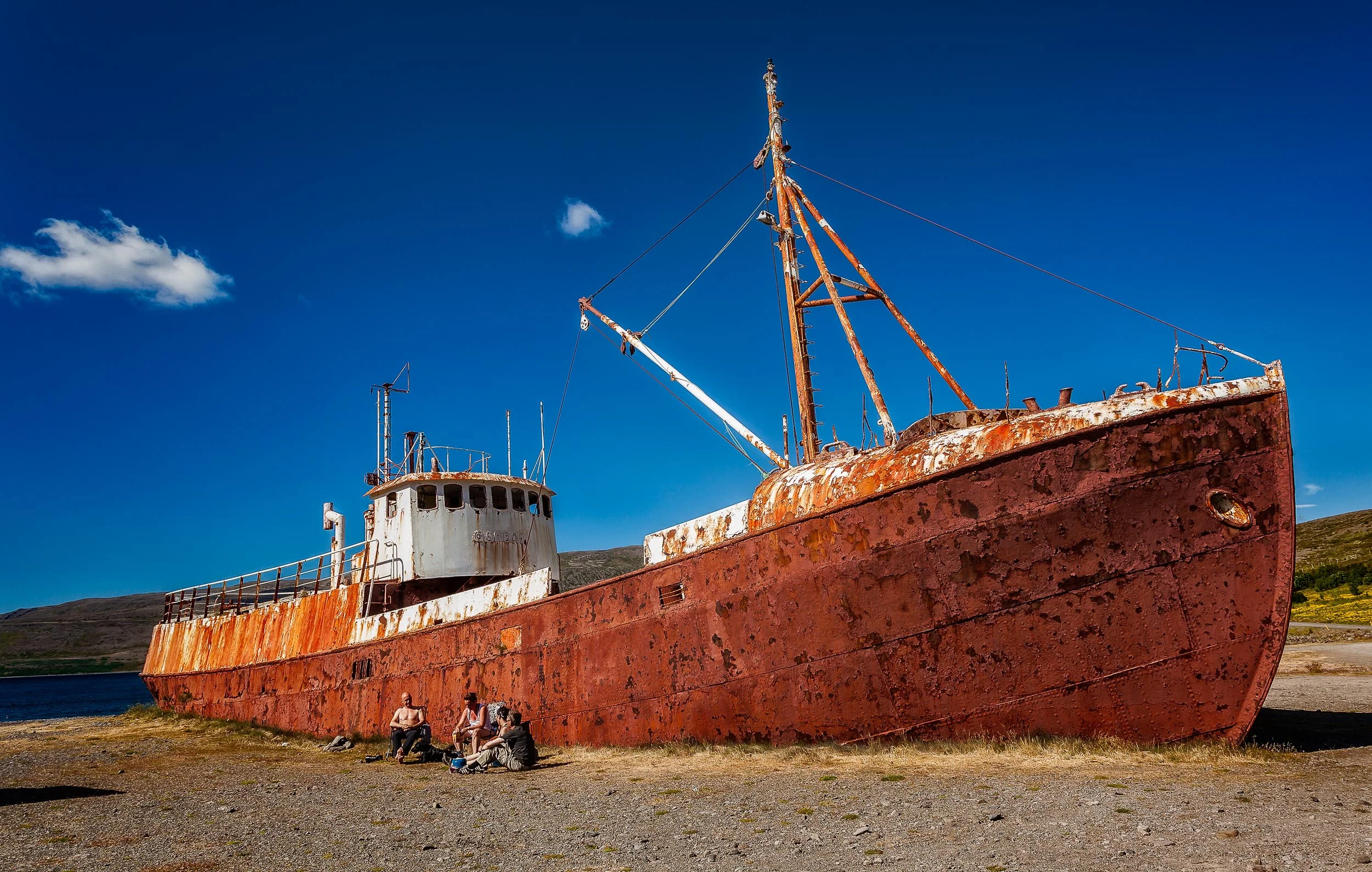 A surreal scene showing some local folk enjoying the sunshine, in front of a beached ship , on a beautiful summer's day in northern Iceland .