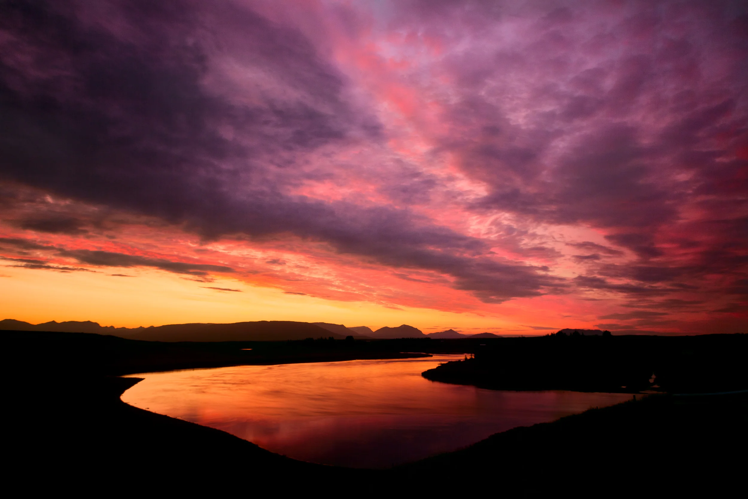 A spectacular sunset , after sinking just below the horizon, produces an amazing afterglow as it illuminates low lying clouds and a small lake on a farm in southern Iceland .