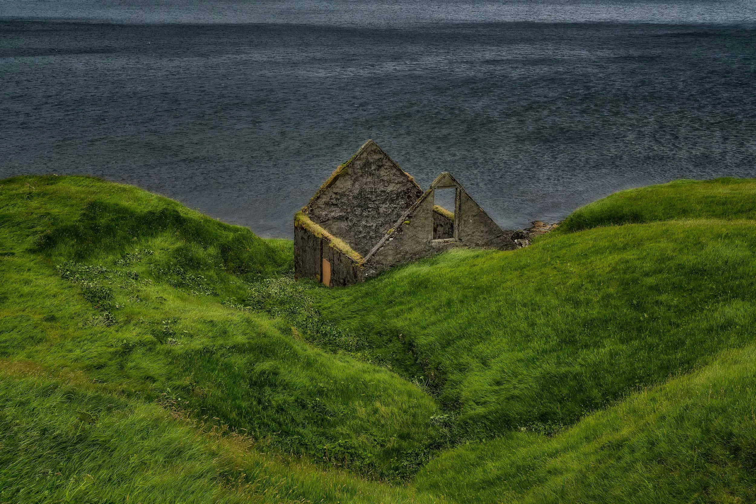 The ruins of a house by the shores of the sea on the island of Eysturoy in the Faroe Islands .