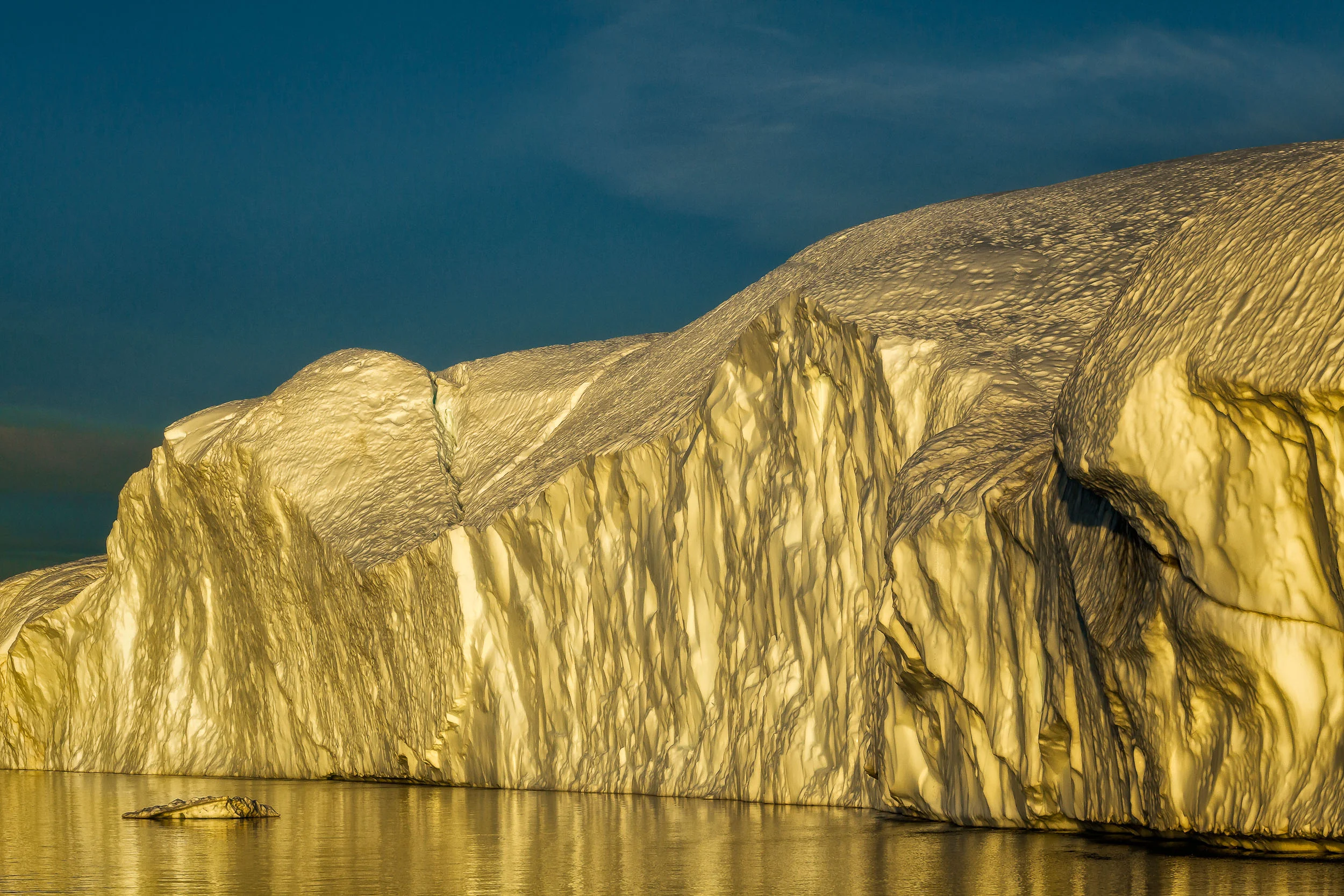 Golden light reflects off a huge iceberg during a Midnight Cruise on a long Summer's night on the Ilulissat Icefjord in Disko Bay, Ilulissat, Greenland