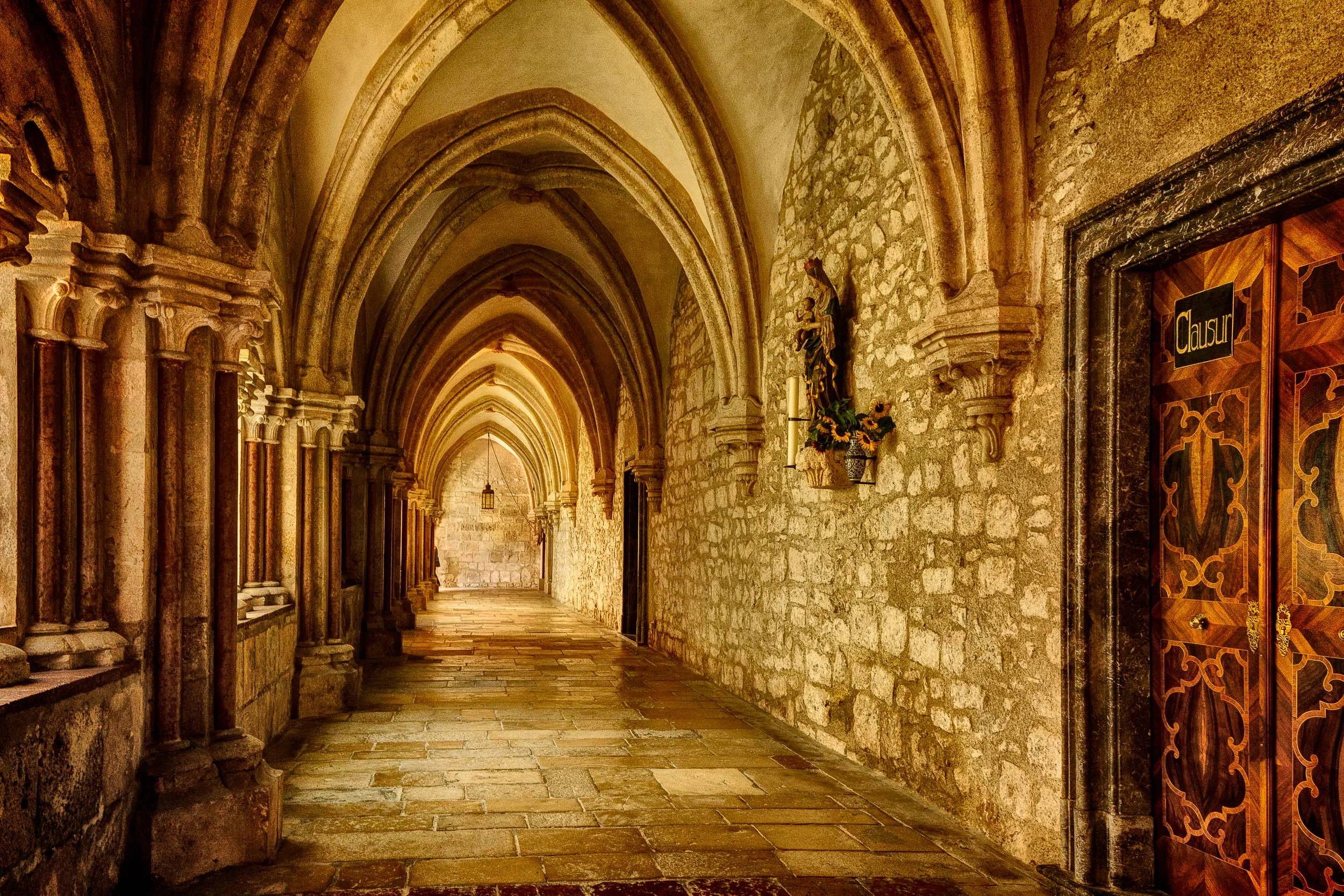 A view down a stone corridor at Helligenkreuz Abbey in Austria . This image is based around the notion of harmonious color .