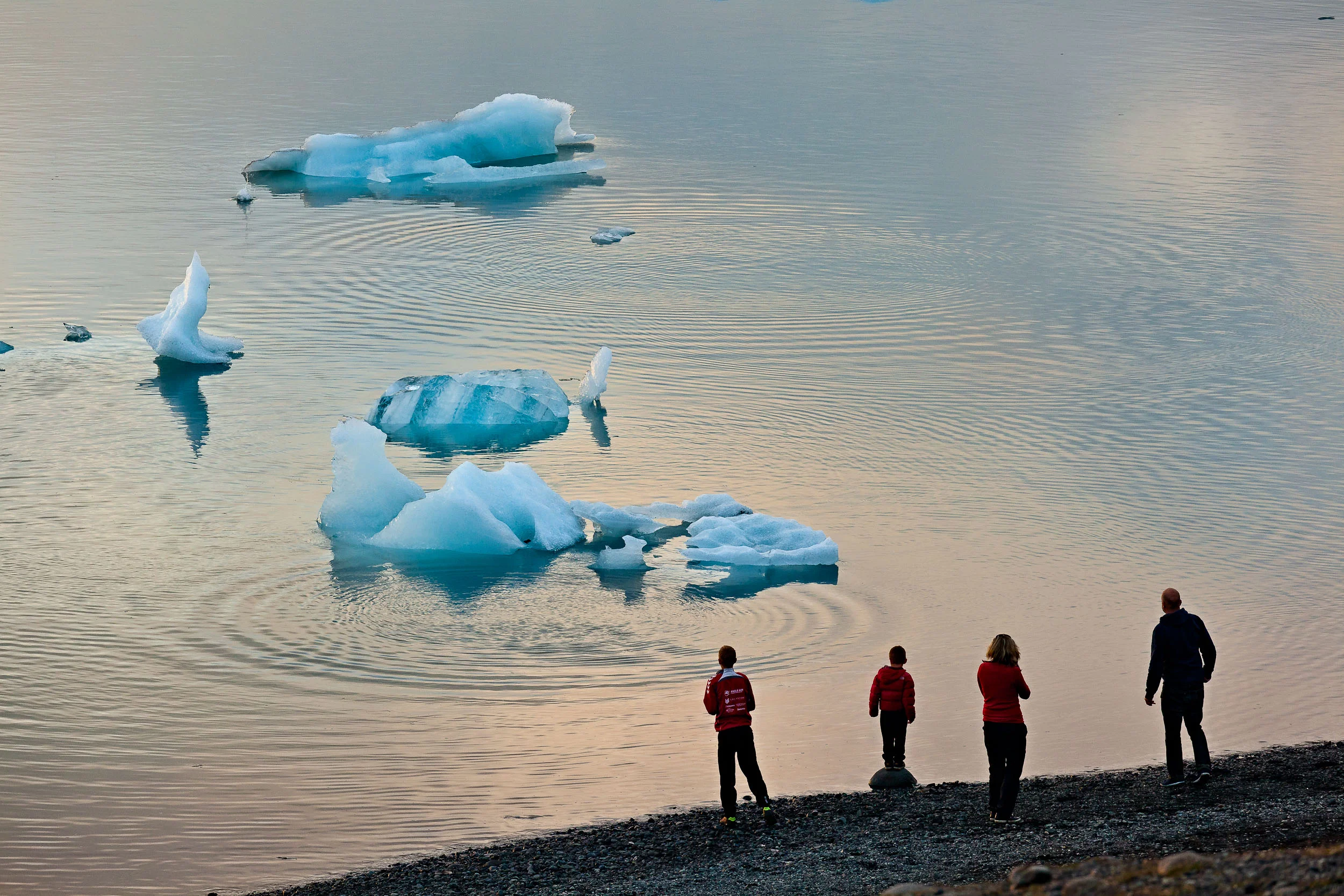 A family watching the breaking up of an iceberg from the shore of the incredible Jokulsarlon Glacier Lagoon in Southern Iceland .