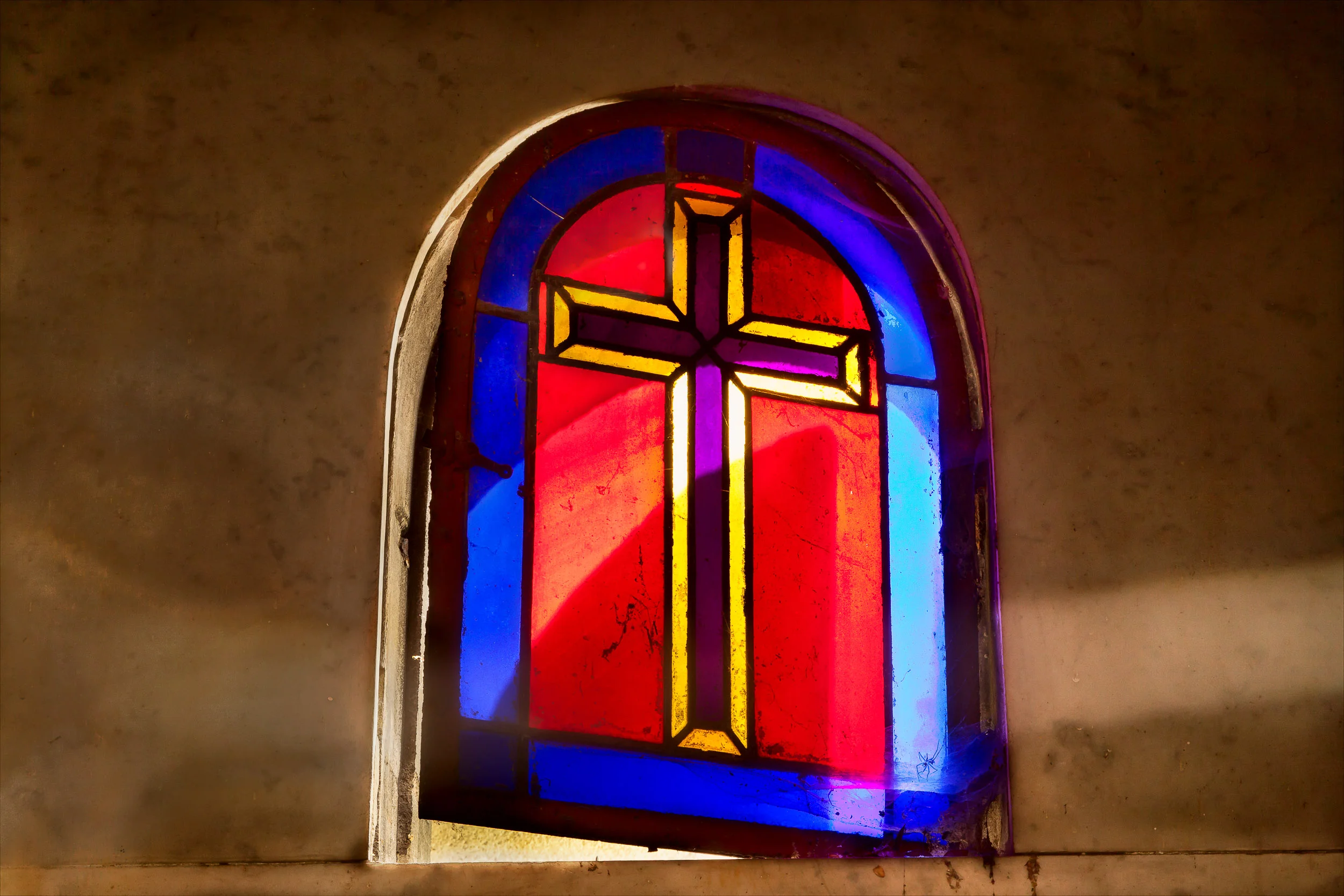 Light passes through a stained glass window , featuring an illustration of the Christian cross , at Père Lachaise Cemetery in Paris, France .
