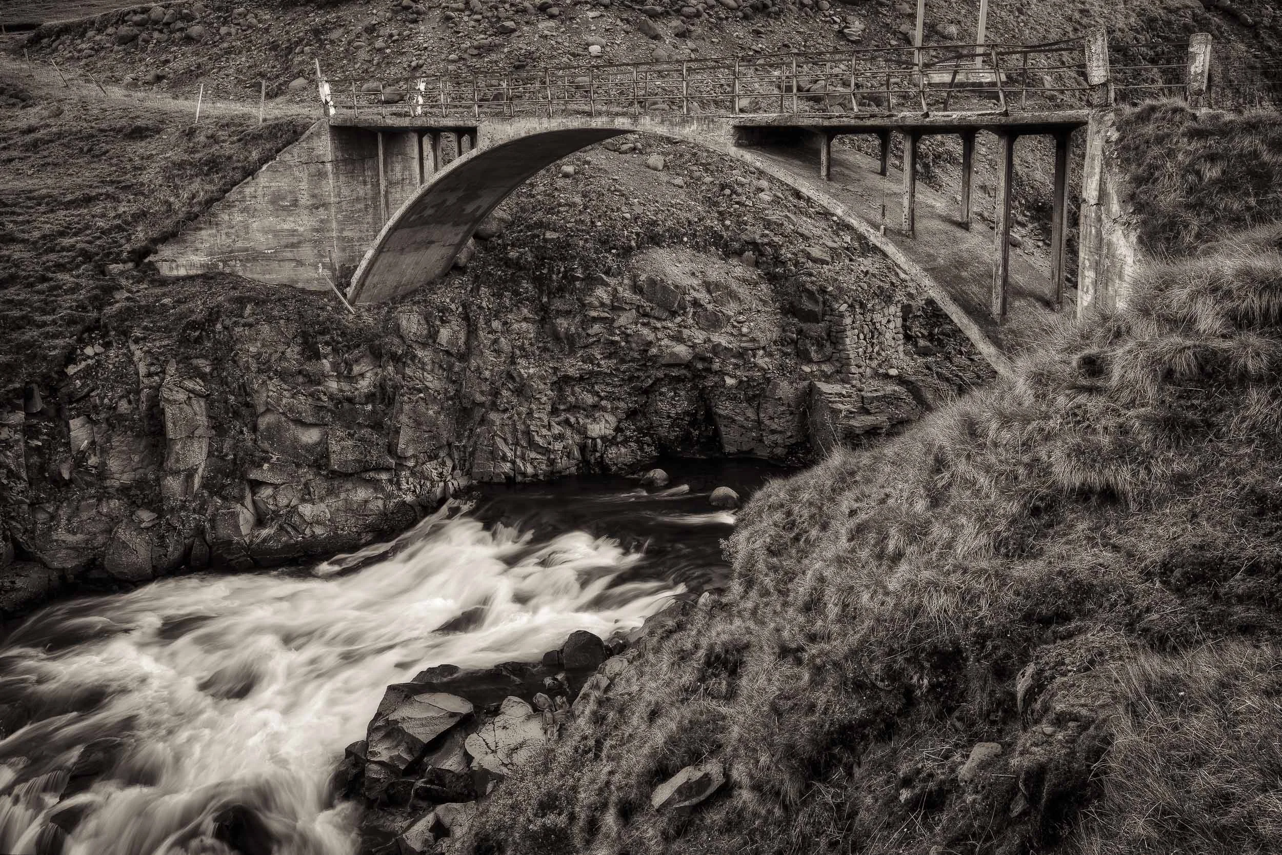 An old stone bridge spanning a fast moving stream in rural Iceland.