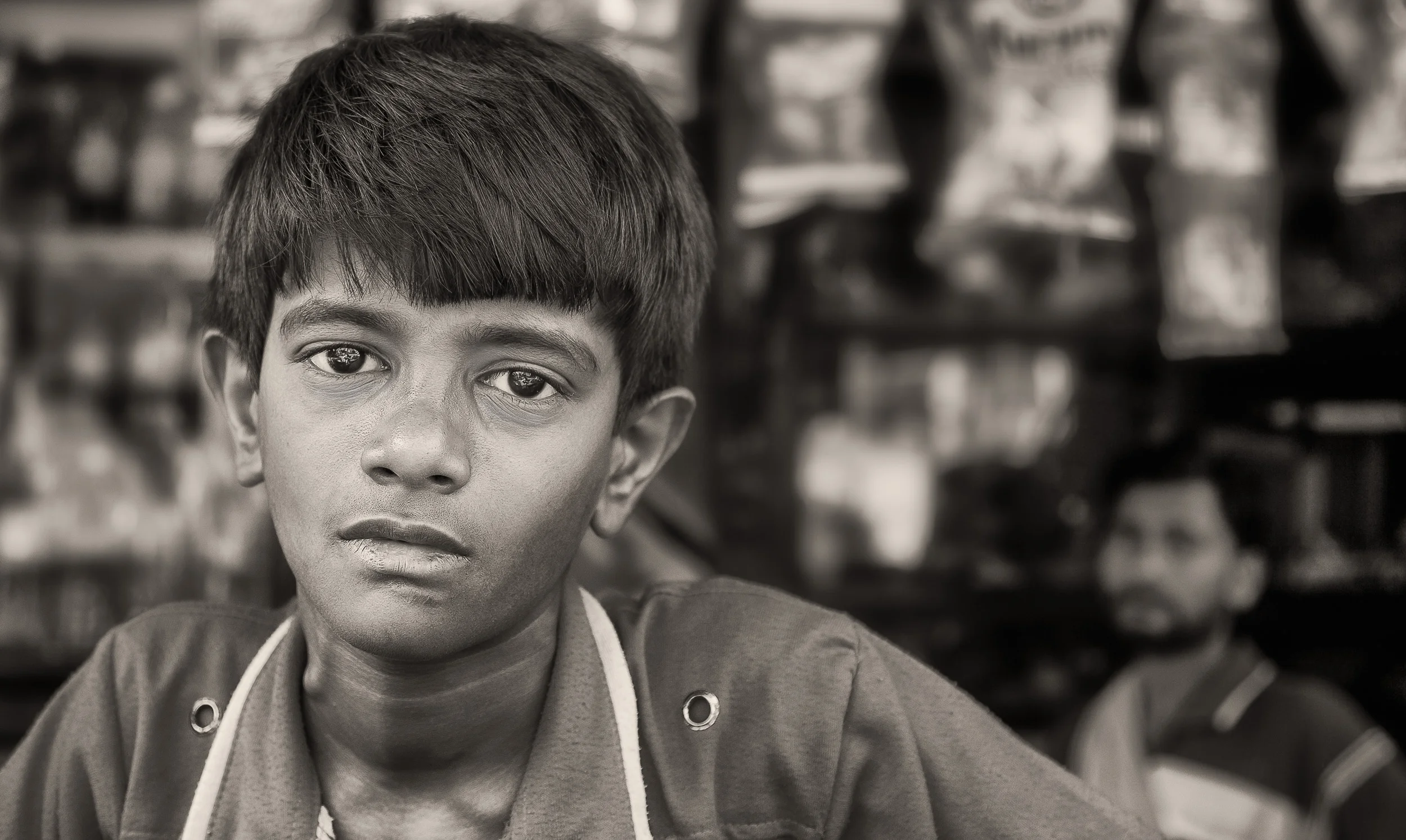 A portrait of a young boy with his father watching on in front of their store in Kolkata, India .