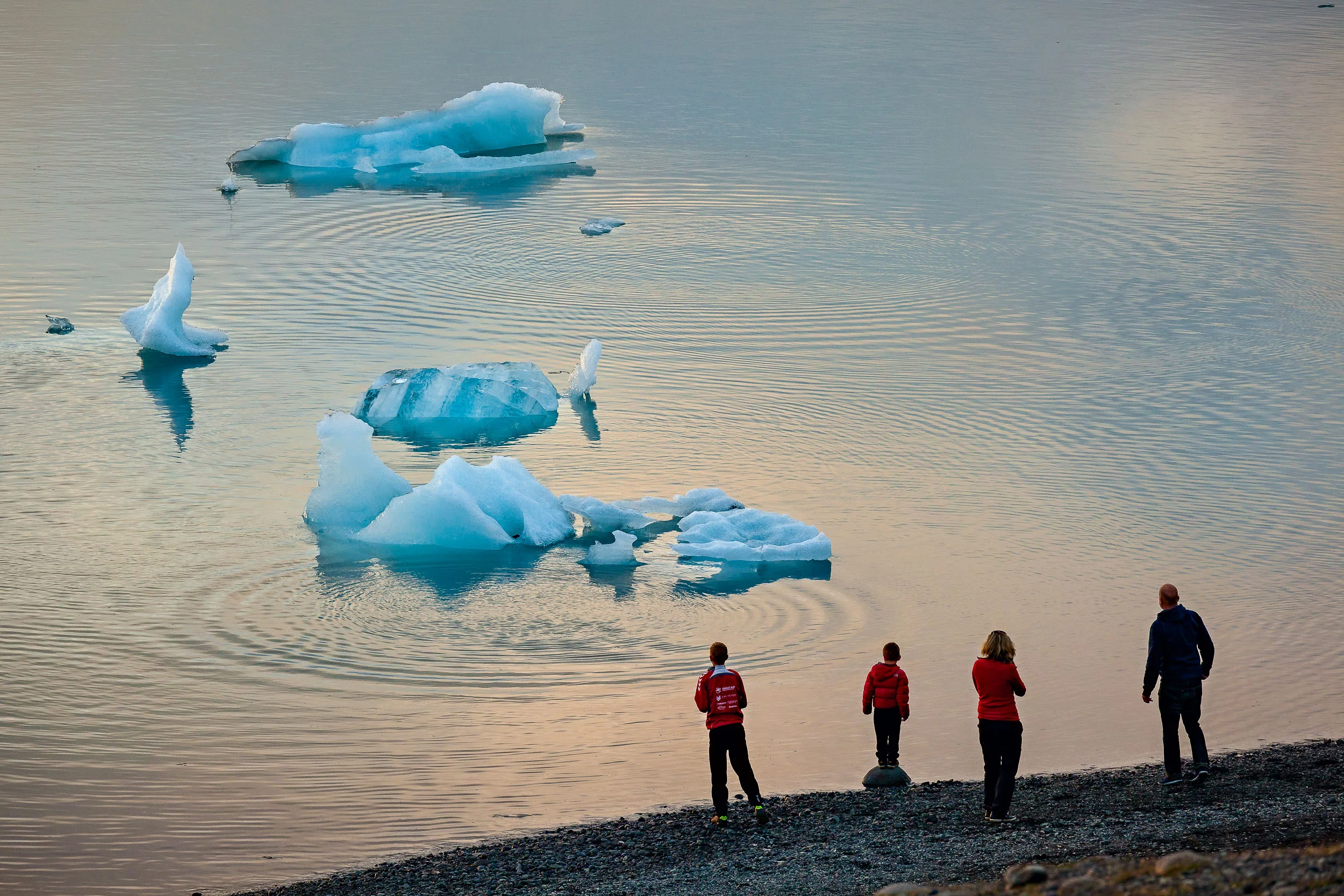 A family watching the breaking up of an iceberg from the shore of the incredible Jökulsárlón Glacier Lagoon in southern Iceland .