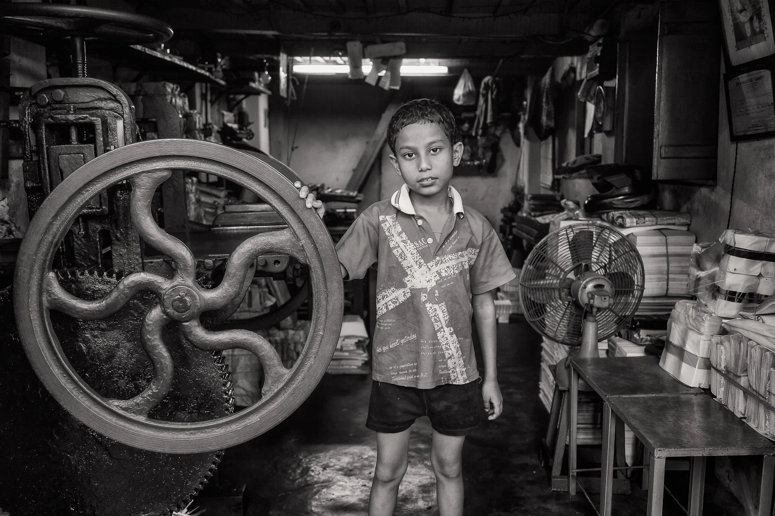 A lovely environmental portrait , in black and white, of a young boy in his father's print workshop in Kolkata, India .