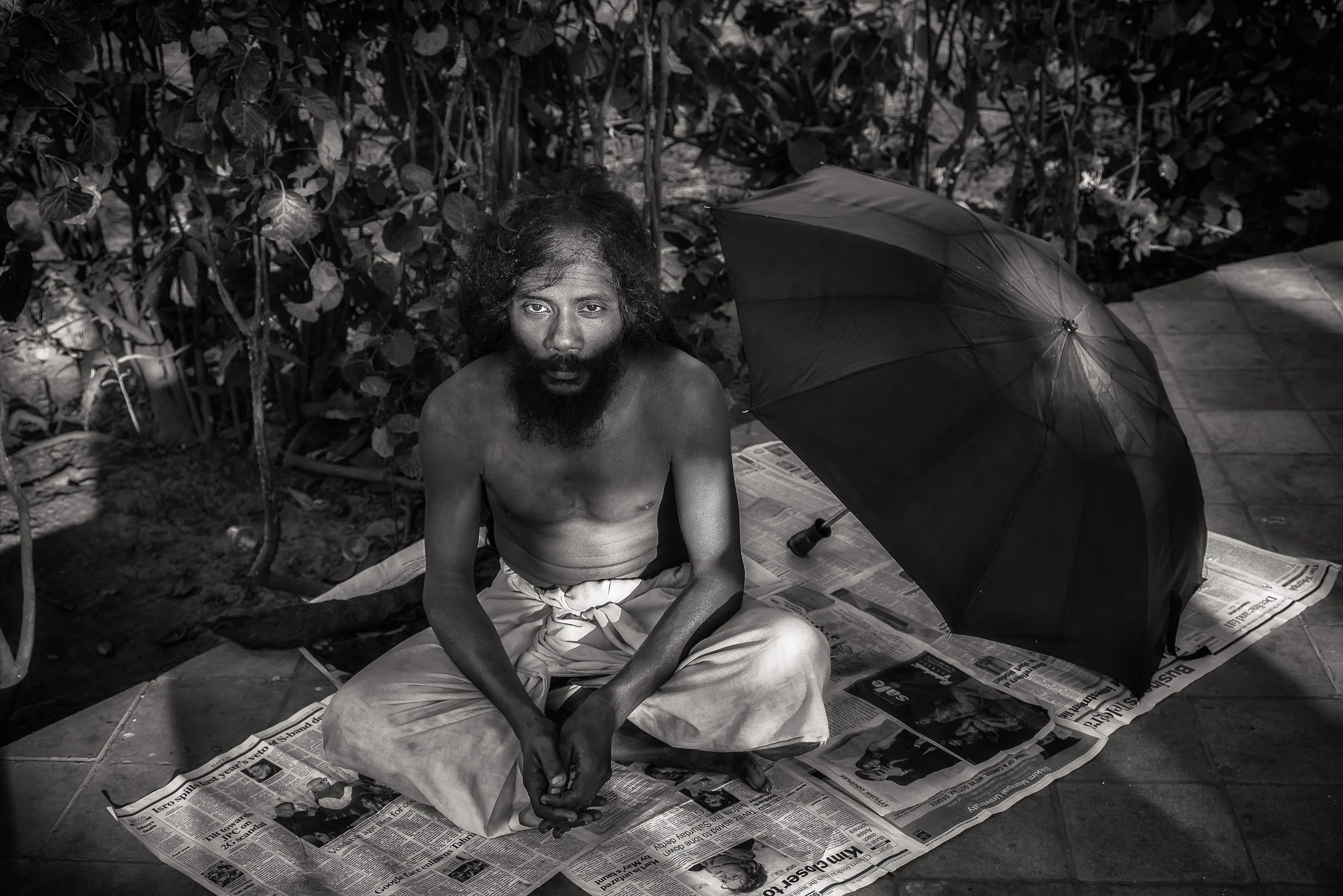 Black and white portrait of a yogi resting in the grounds of a temple complex by the banks of the Hooghly River in Kolkata, India .