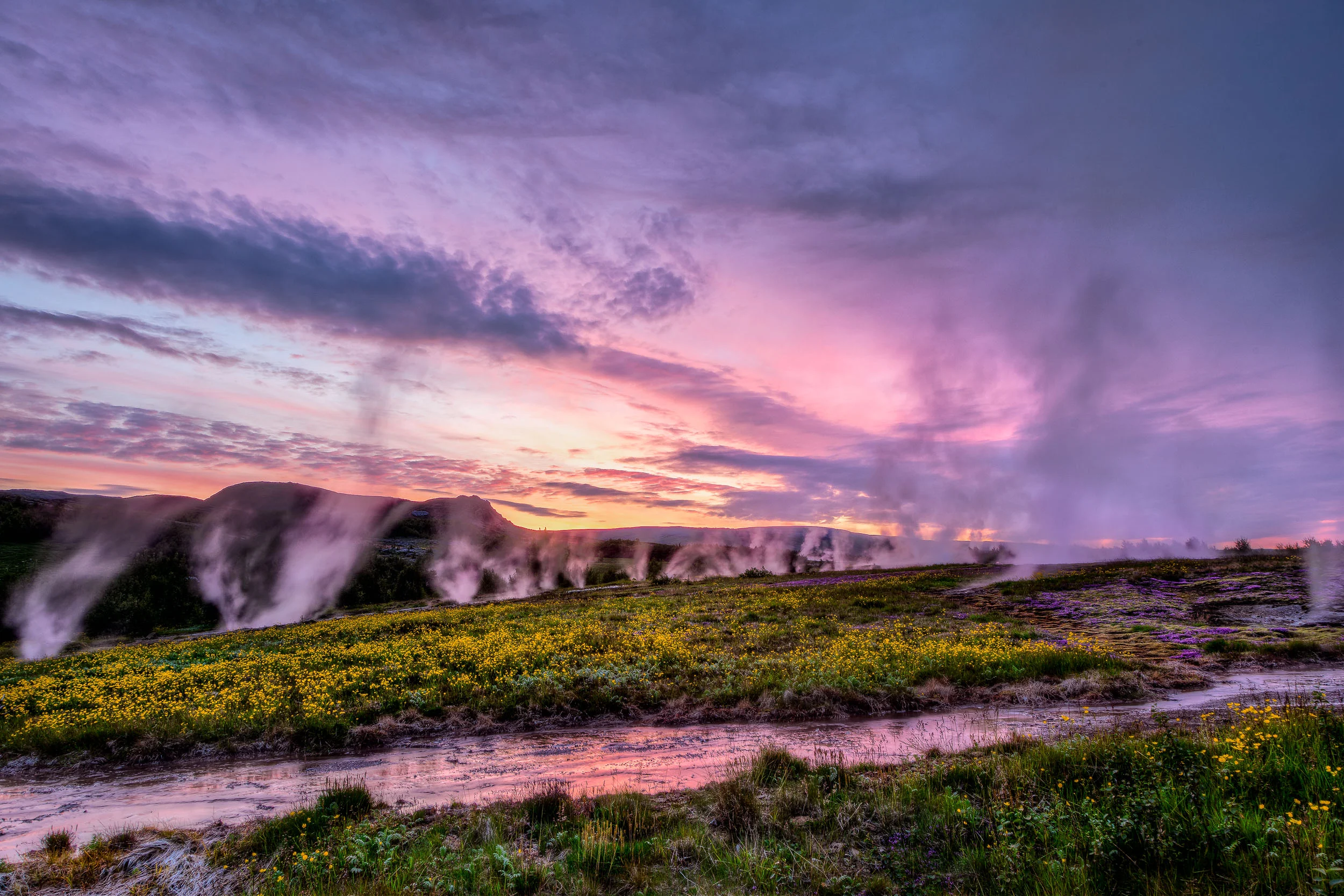 A purple and pink sky reflected in a stream at sunset while hot springs vent steam into the air in Iceland, the land of ice and fire .