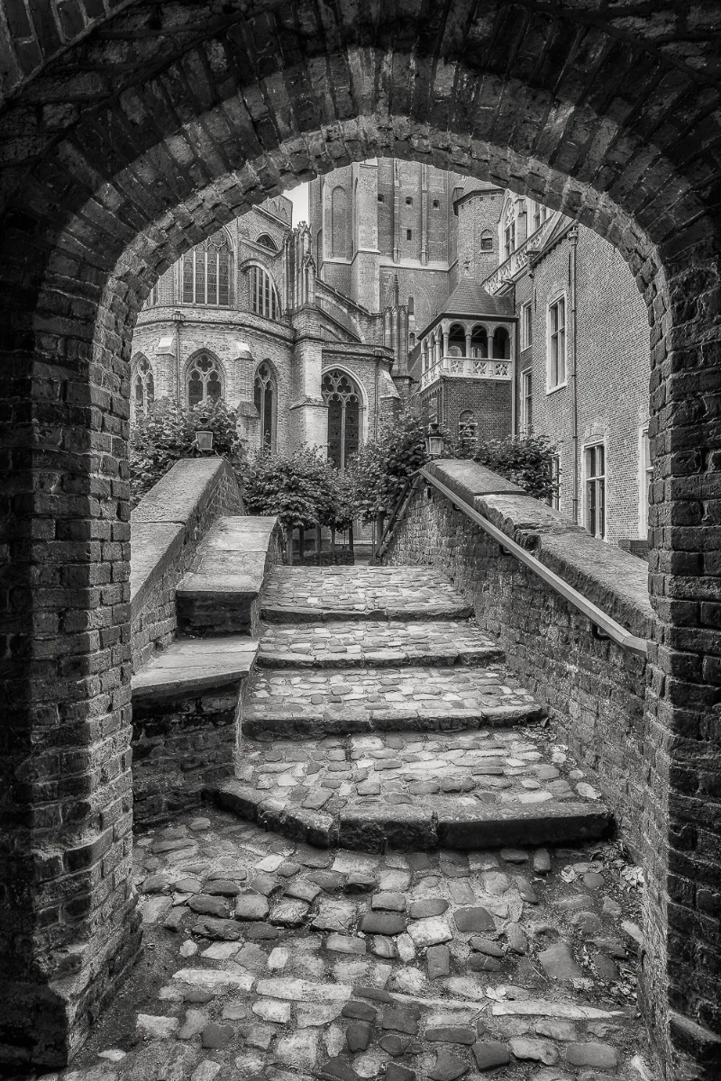 A classic view looking through an archway onto a bridge and onwards towards historic buildings in Bruges, Belgium .