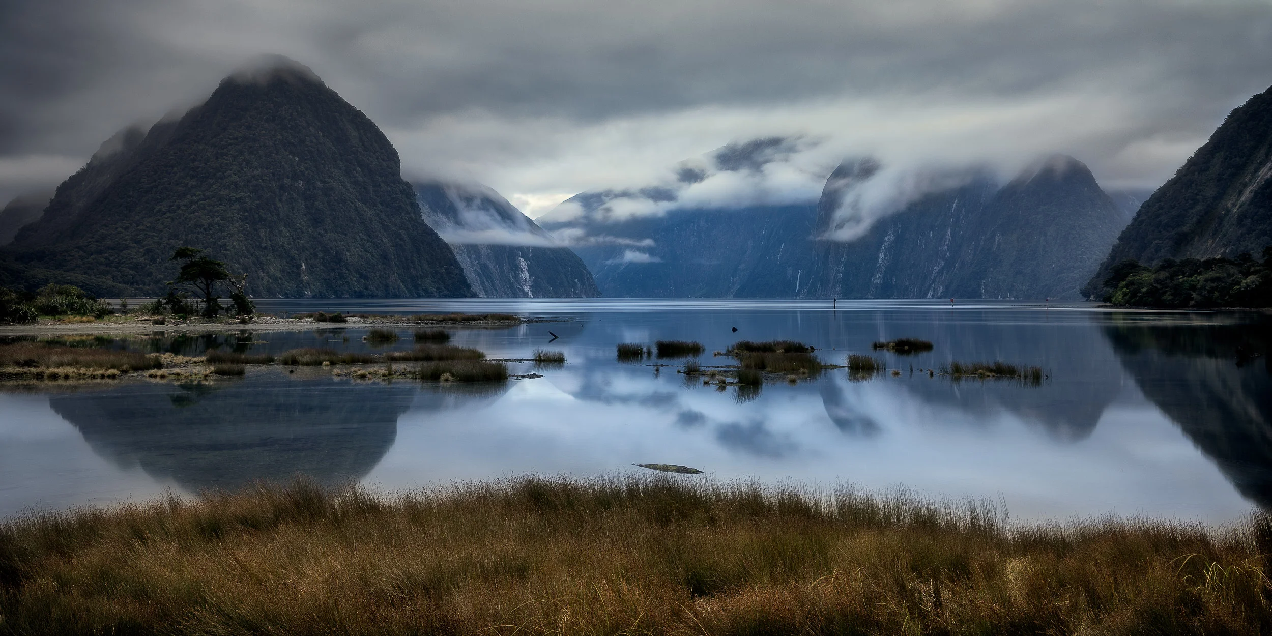 The blue light of dawn on a still morning at Milford Sound, New Zealand .