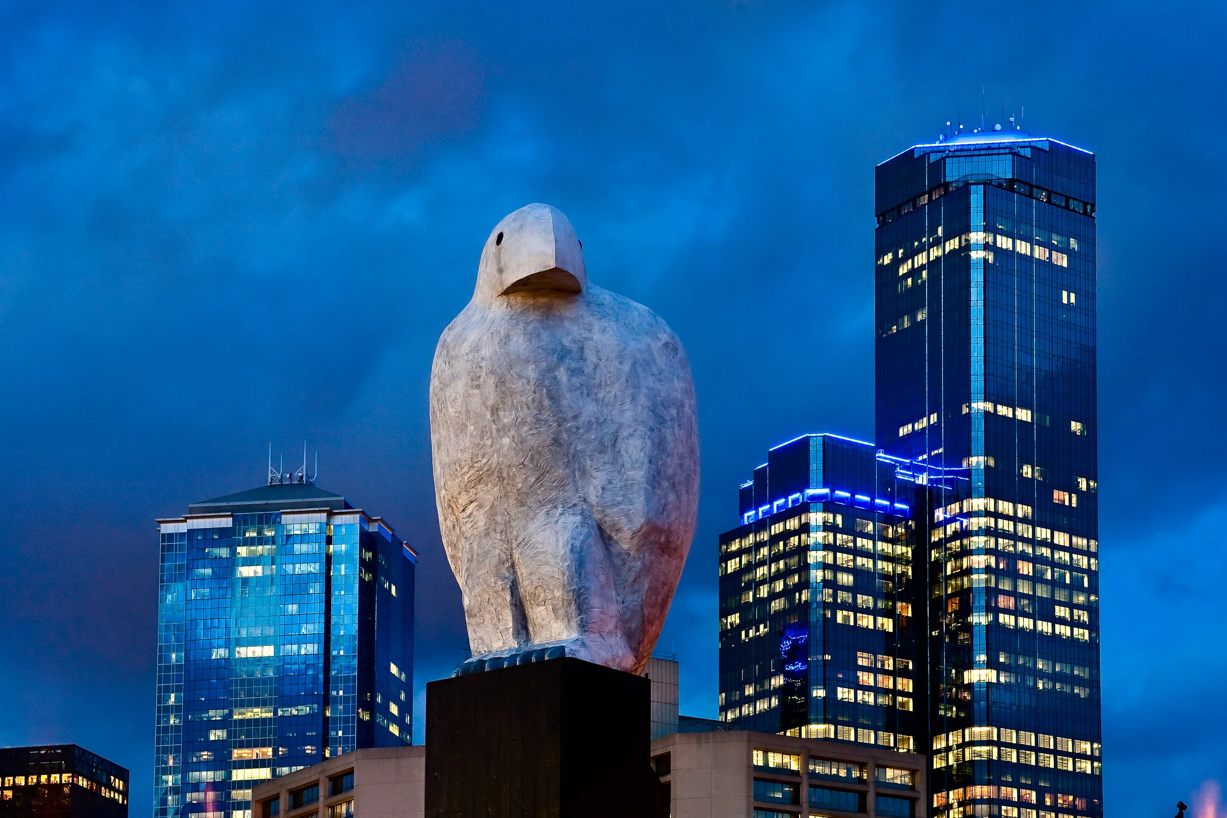 A giant owl statue perched high amidst the Melbourne skyline .