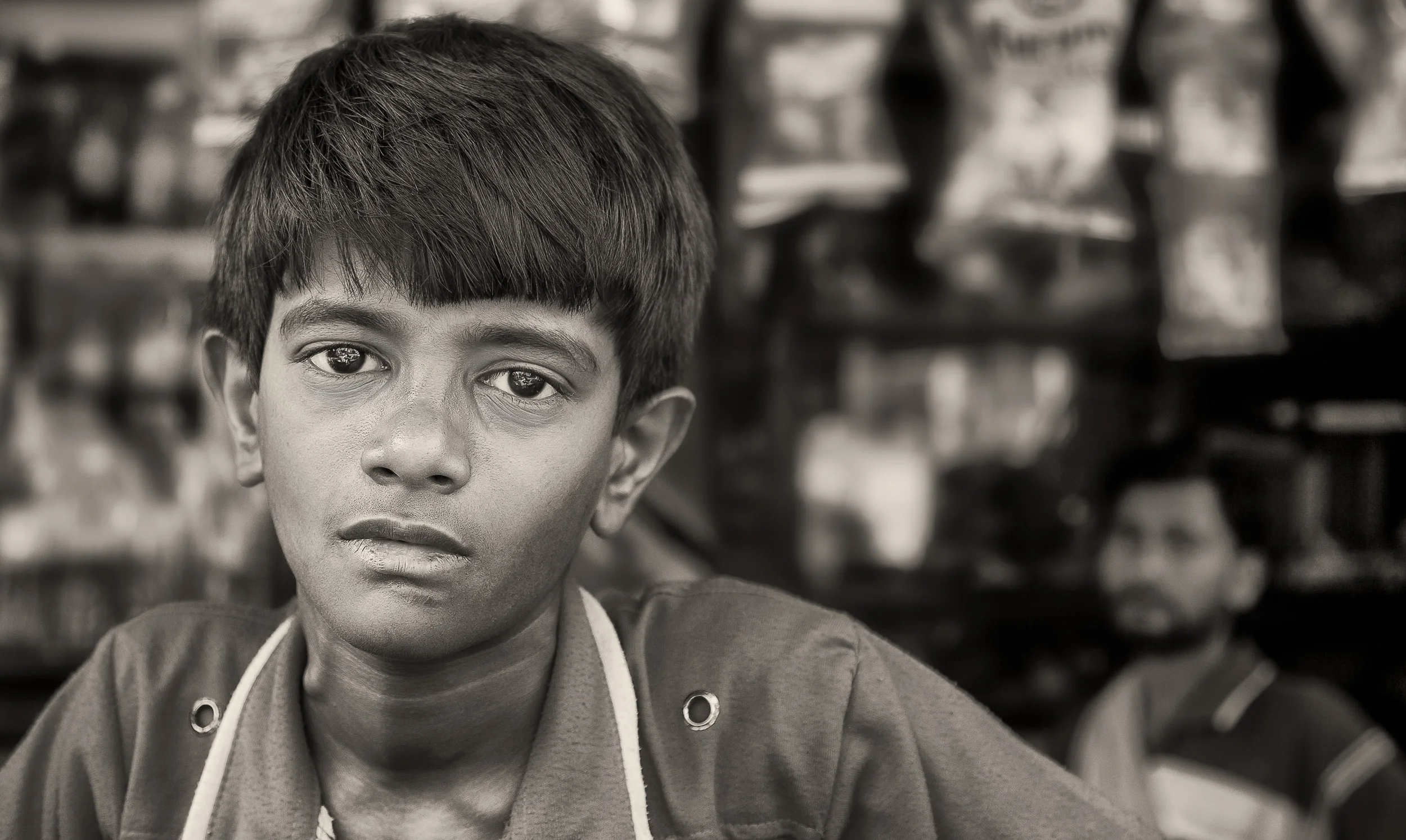 A portrait of a young boy with his father watching on in front of their store in Kolkata, India .