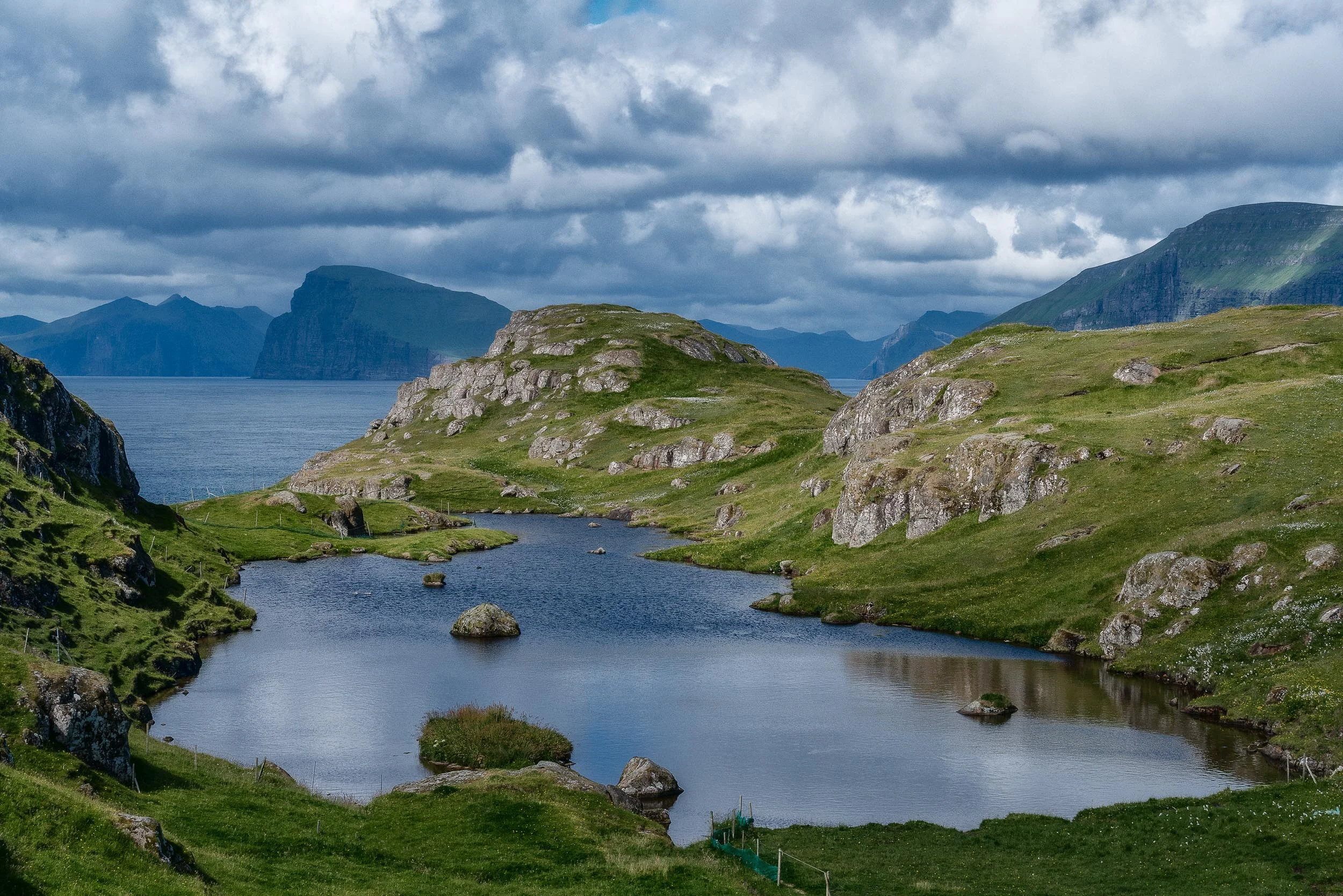 Green rocky terrain and blue waters, underneath a stormy sky, provide an incredibly beautiful outlook near the town of Skopun on the island of Sandoy in the Faroe Islands .