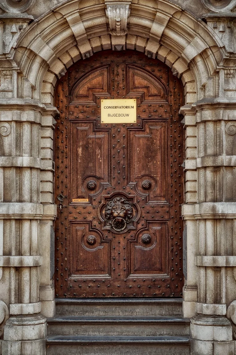 A highly detailed door , beautifully framed in stone, leading into the Conservatorium in Bruges, Belgium .