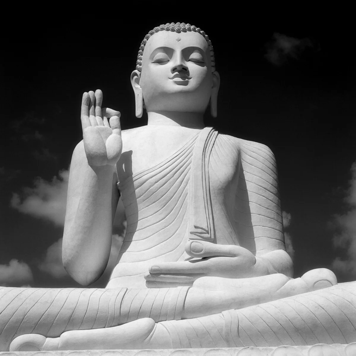A huge Buddha statue , perched high on a hilltop, against a dark sky in Mihintale, Sri Lanka .