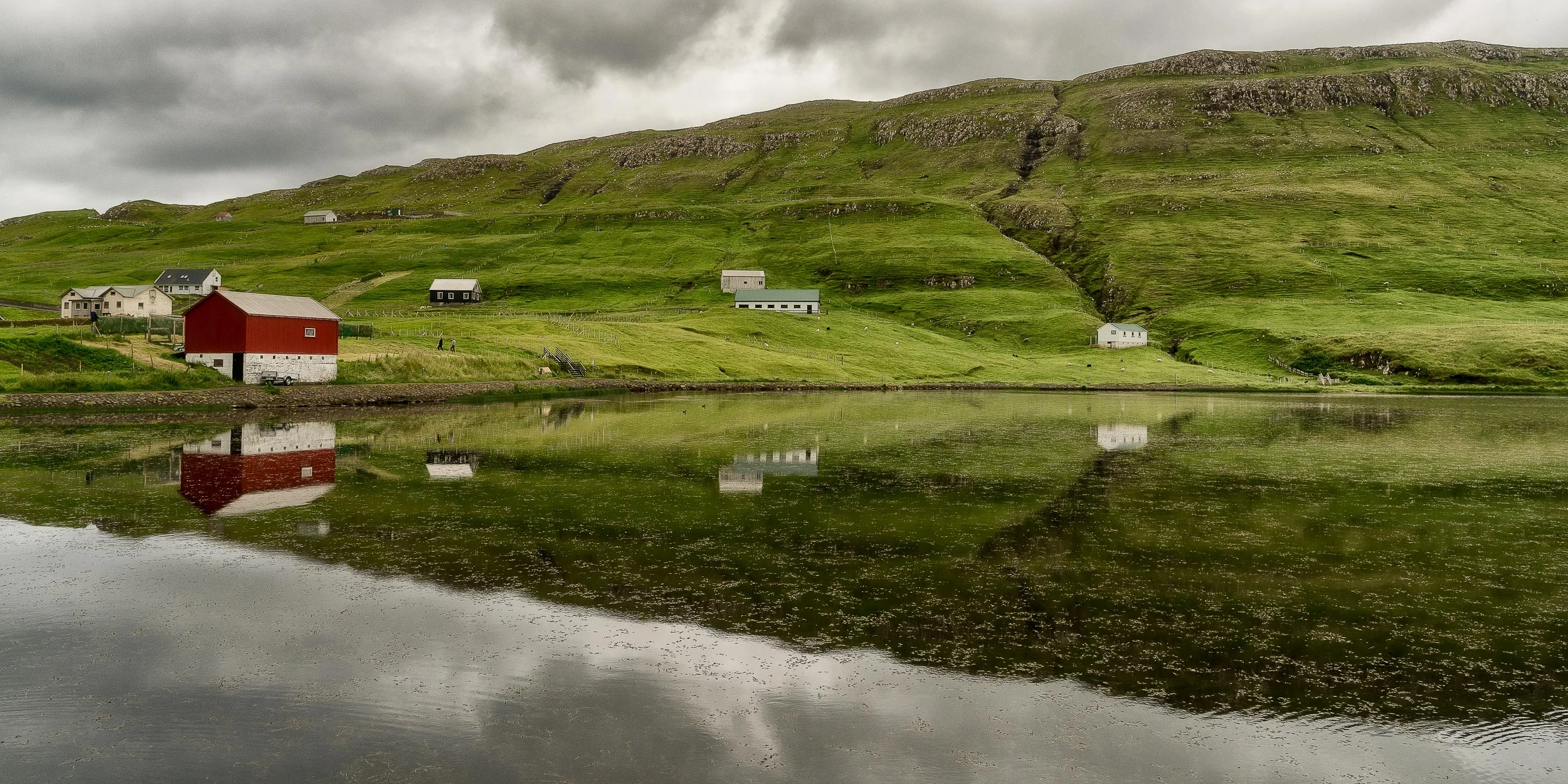 A serene scene of farm houses around the edges of a lake on the island of Suduroy in the Faroe Islands .