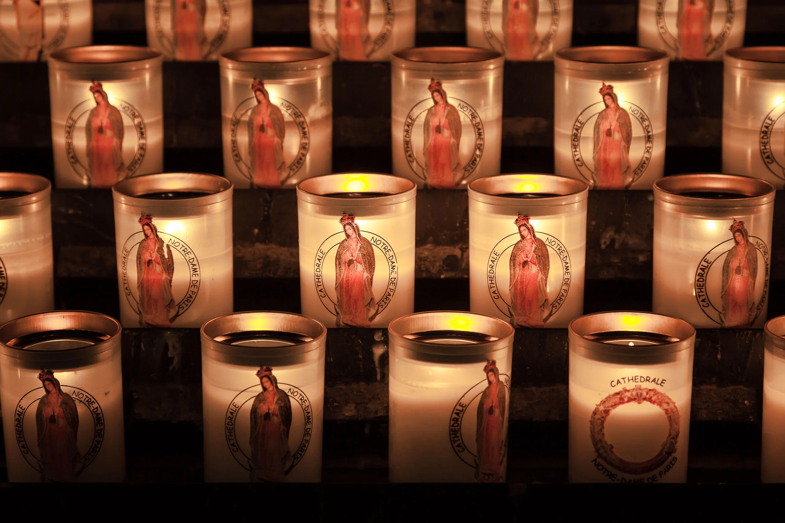 A close up view of candles , featuring the Virgin Mary , inside the Notre Dame Cathedral in Paris, France with a more antique rendering of color .