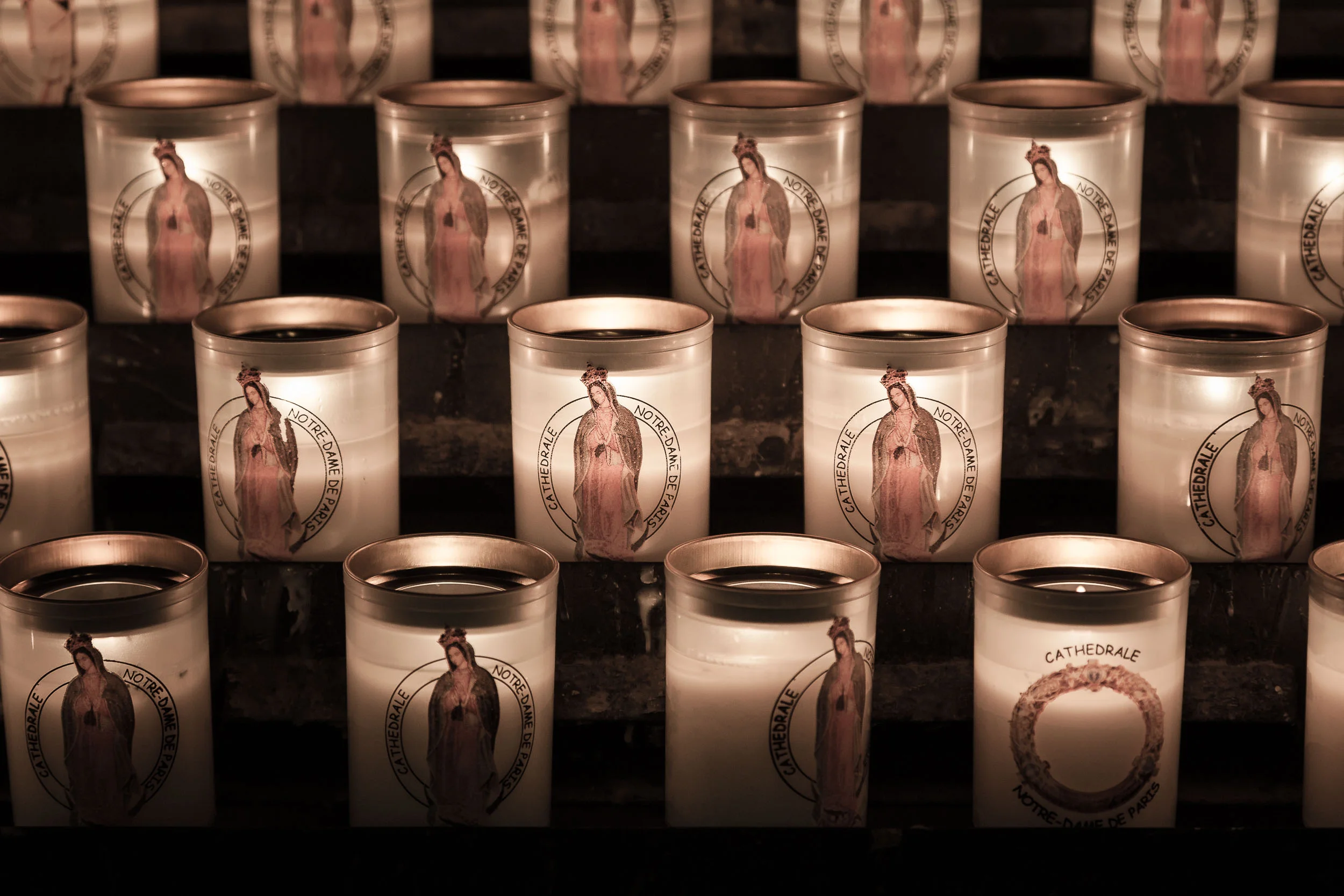 A close up view of candles , featuring the Virgin Mary , inside the Notre Dame Cathedral in Paris, France. This version shows a subtle pink color rendering in the candles.