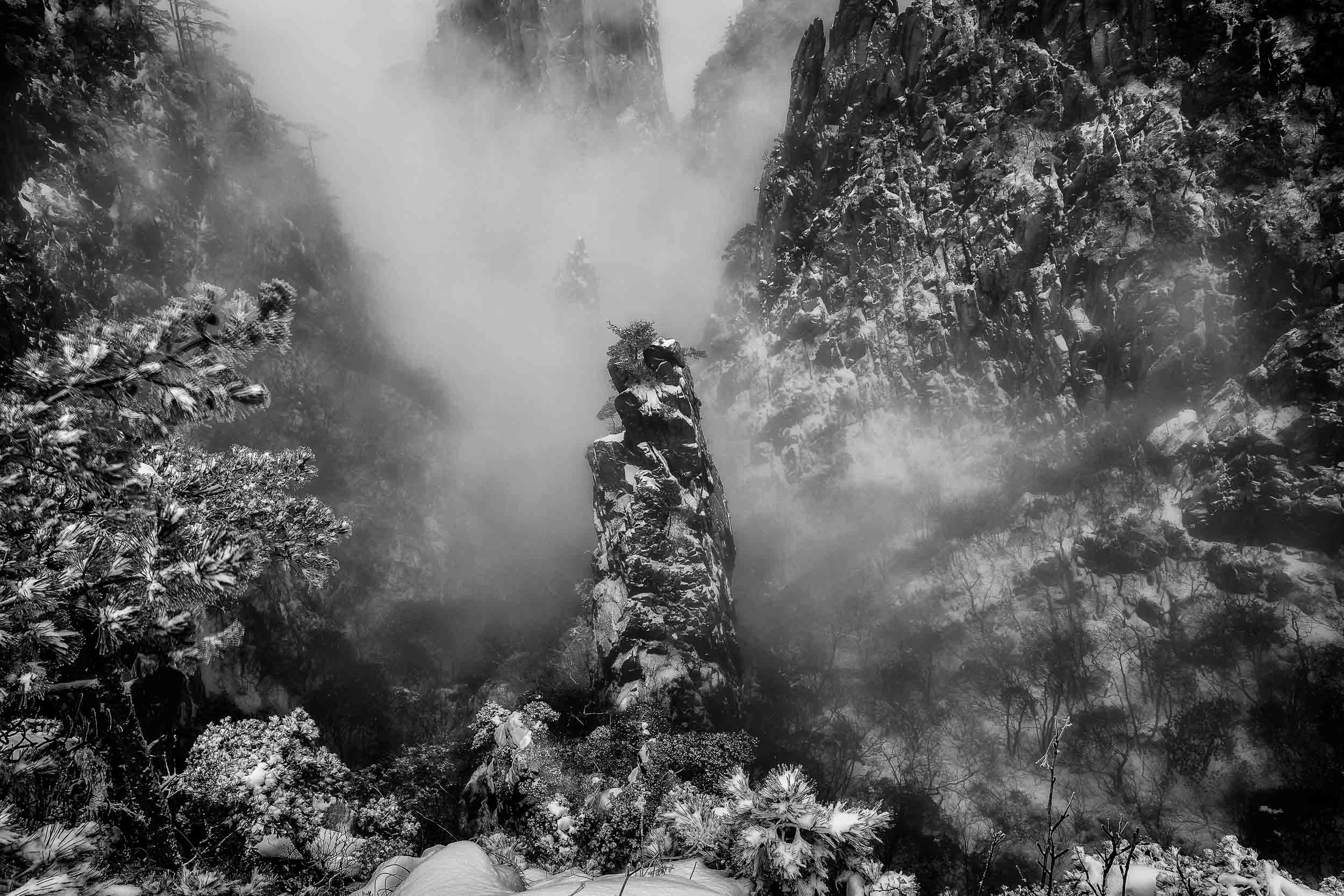 Dramatic photo of mist, swirling around a rock formation, on Huangshan, China.