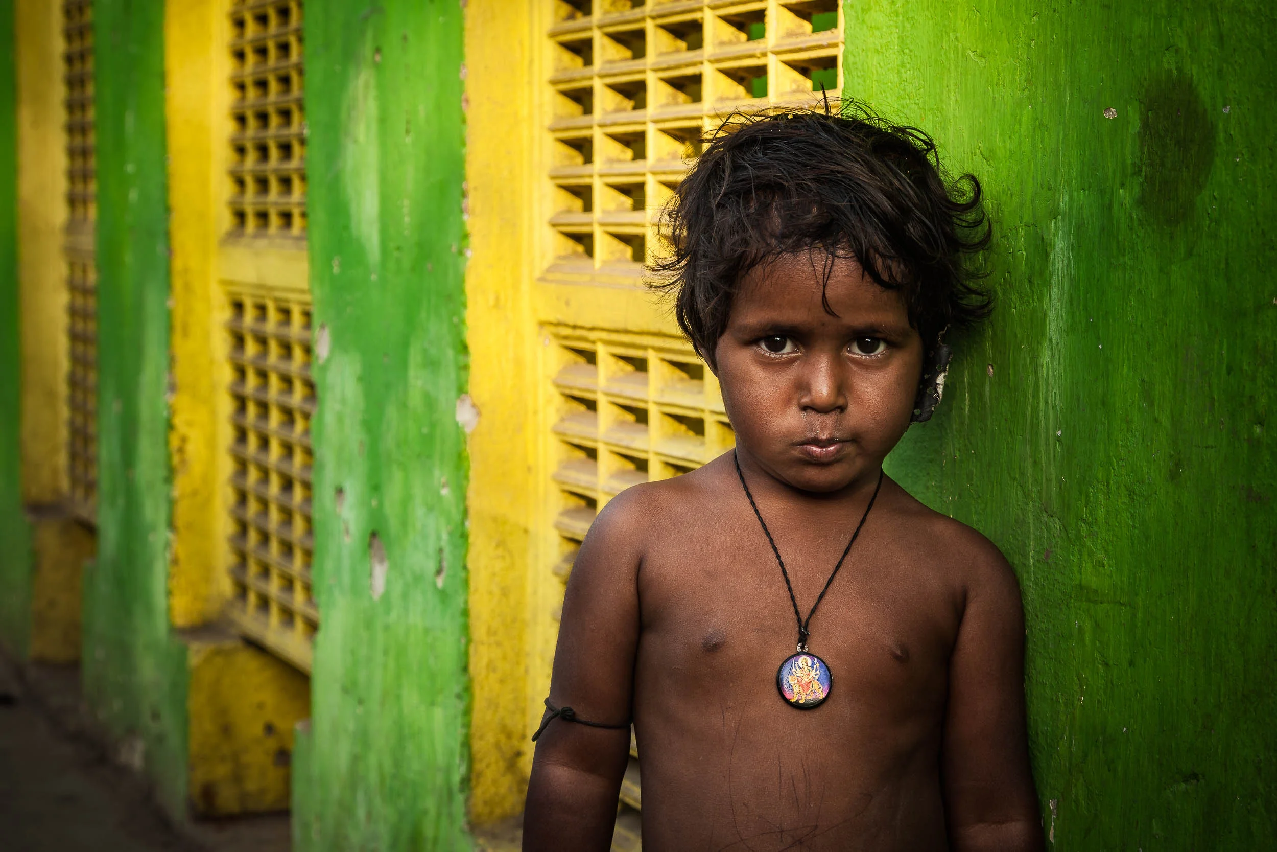 A bright green and yellow wall provides a colorful background for this portrait of a child at a Kolkata railway station in India .