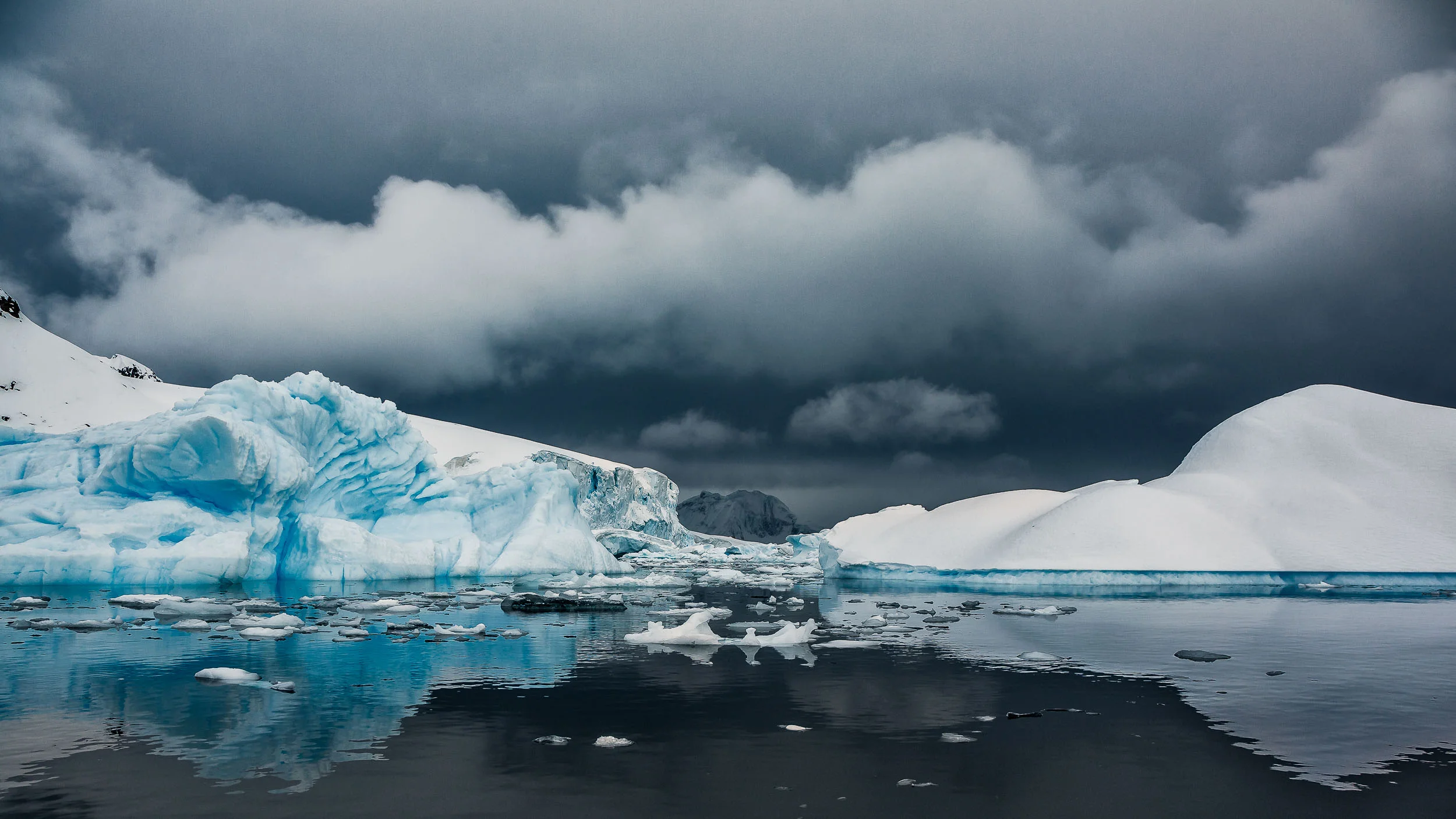 A dramatic sky and calm waters frame masses of ice and snow off Cuverville Island, Antarctica .