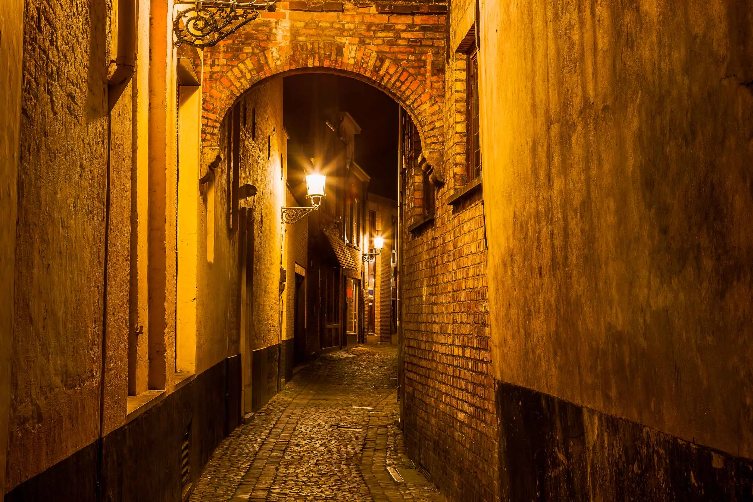 A colorfully lit alleyway , photographed at night, in the city of Bruges (i.e., Brugge), Belgium .