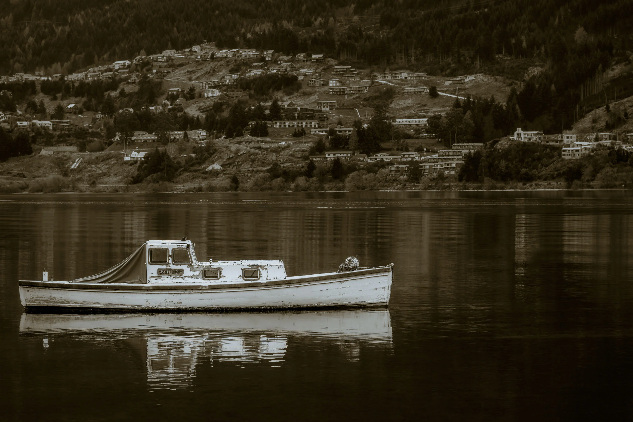 A little boat floats peacefully on Lake Wakatipu in Queenstown, New Zealand .