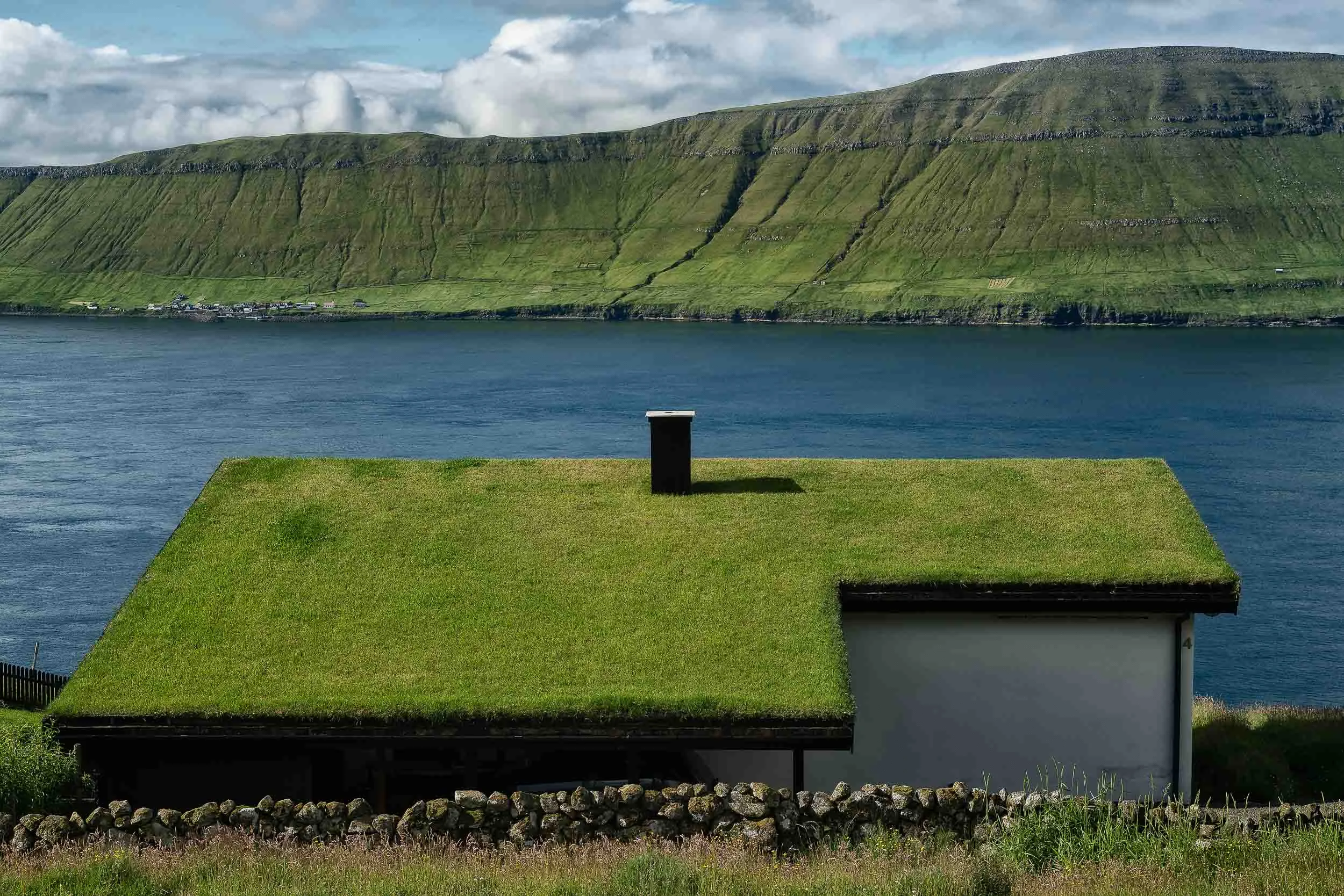 A lush turf roof on an idyllically located house by a fjord on the island of Streymoy in the Faroe Islands .