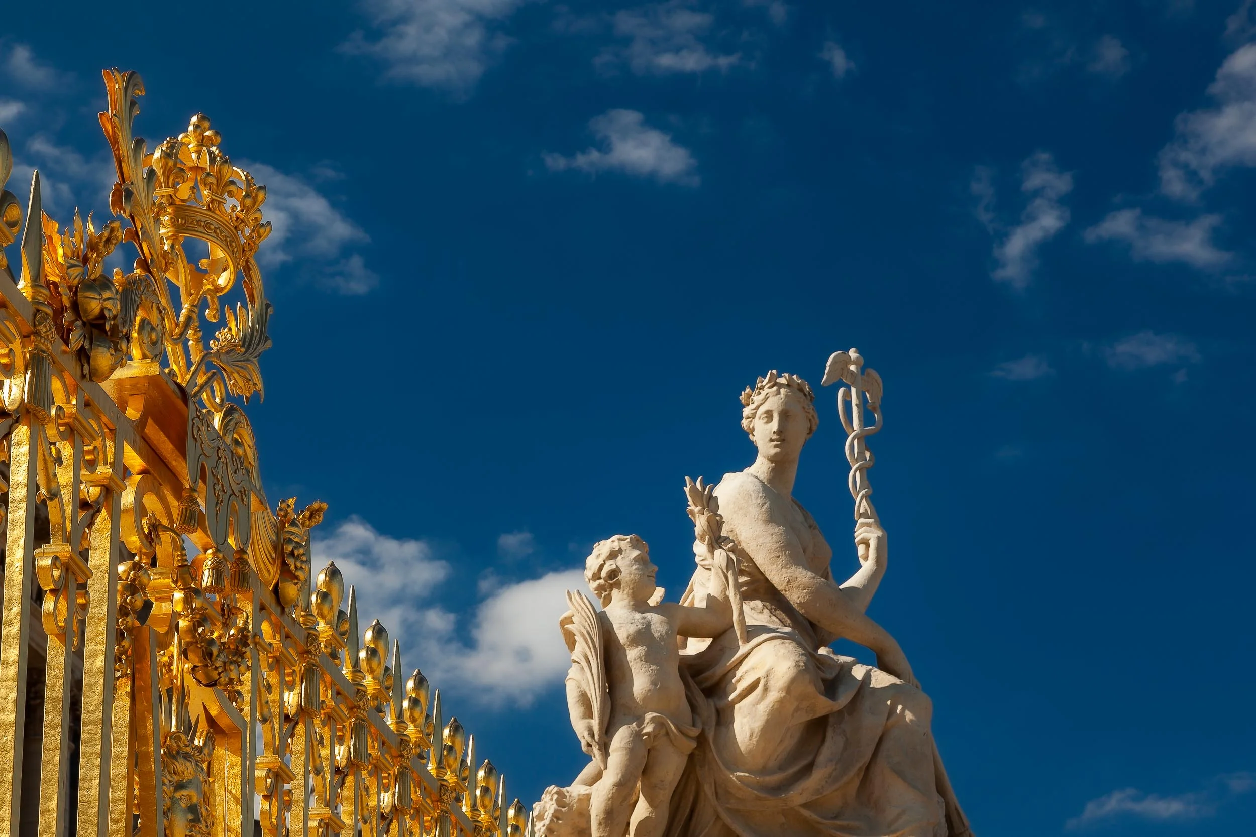 Striking light illuminates statues and the golden gate at the Palace of Versailles, France .