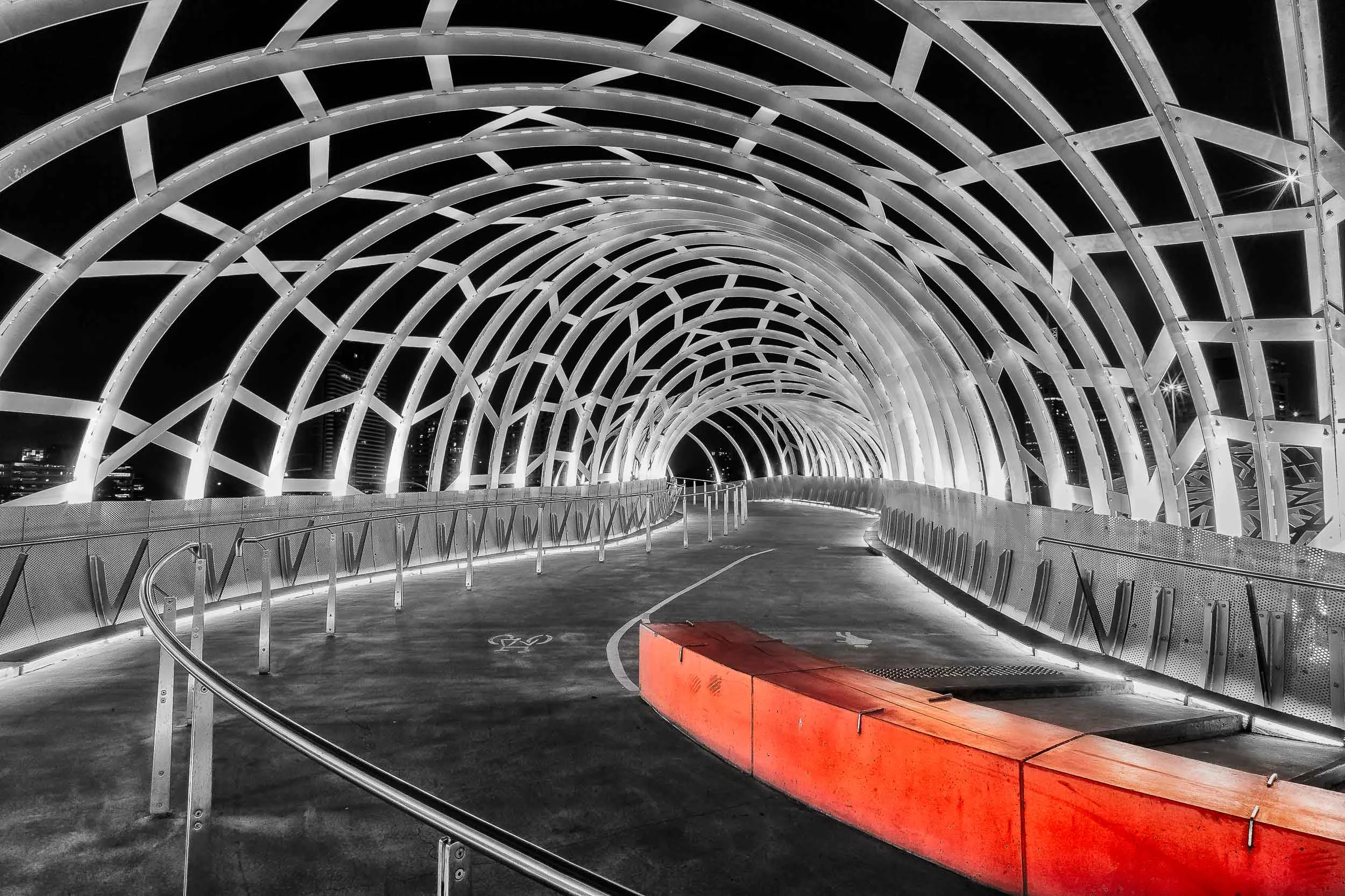 A red barrier provides a splash of vibrant color in this otherwise black and white photo of Web Bridge in the Docklands precinct of Melbourne, Australia .