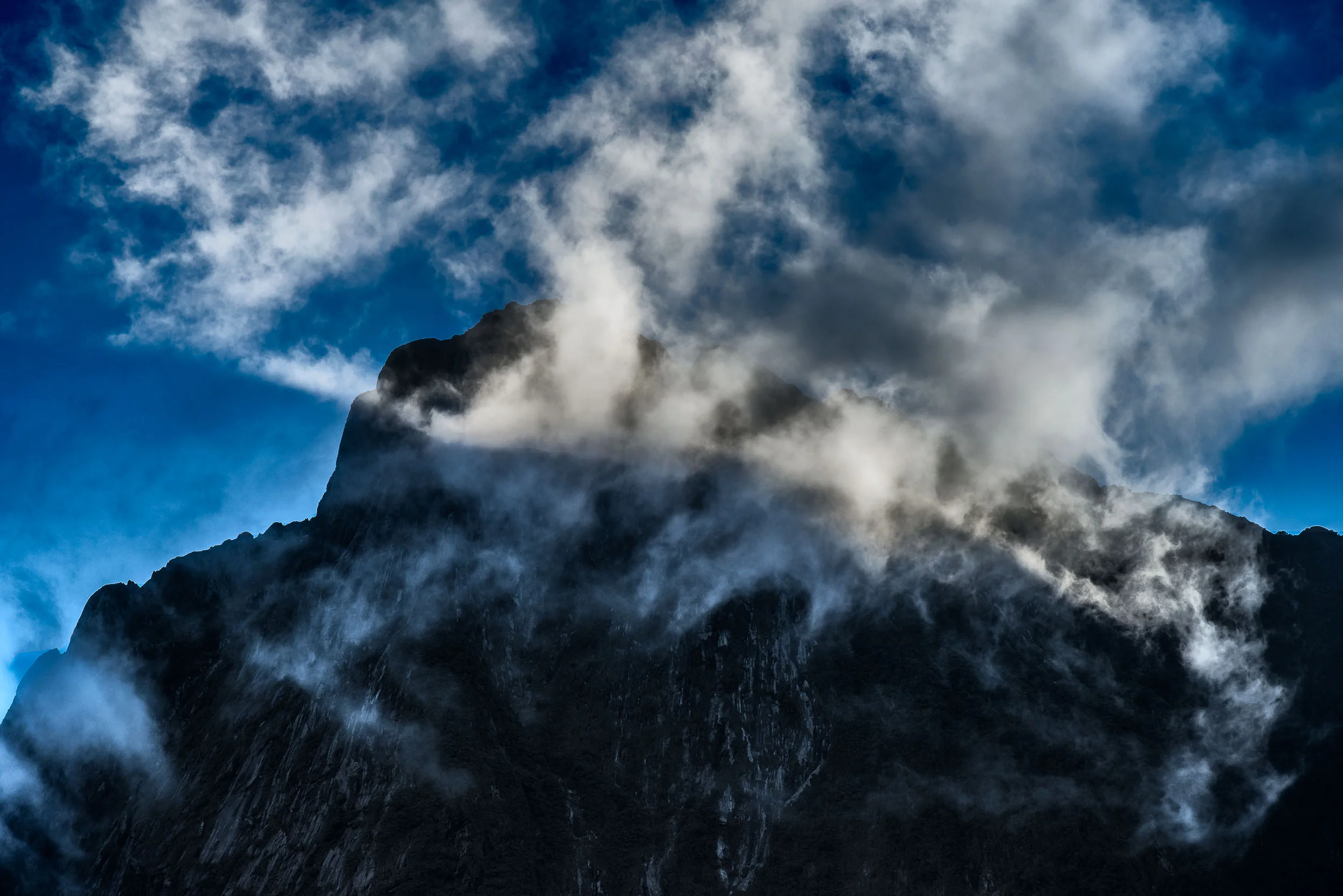 A spectacular scene as light illuminates clouds in front of a mountain top above Milford Sound , New Zealand .