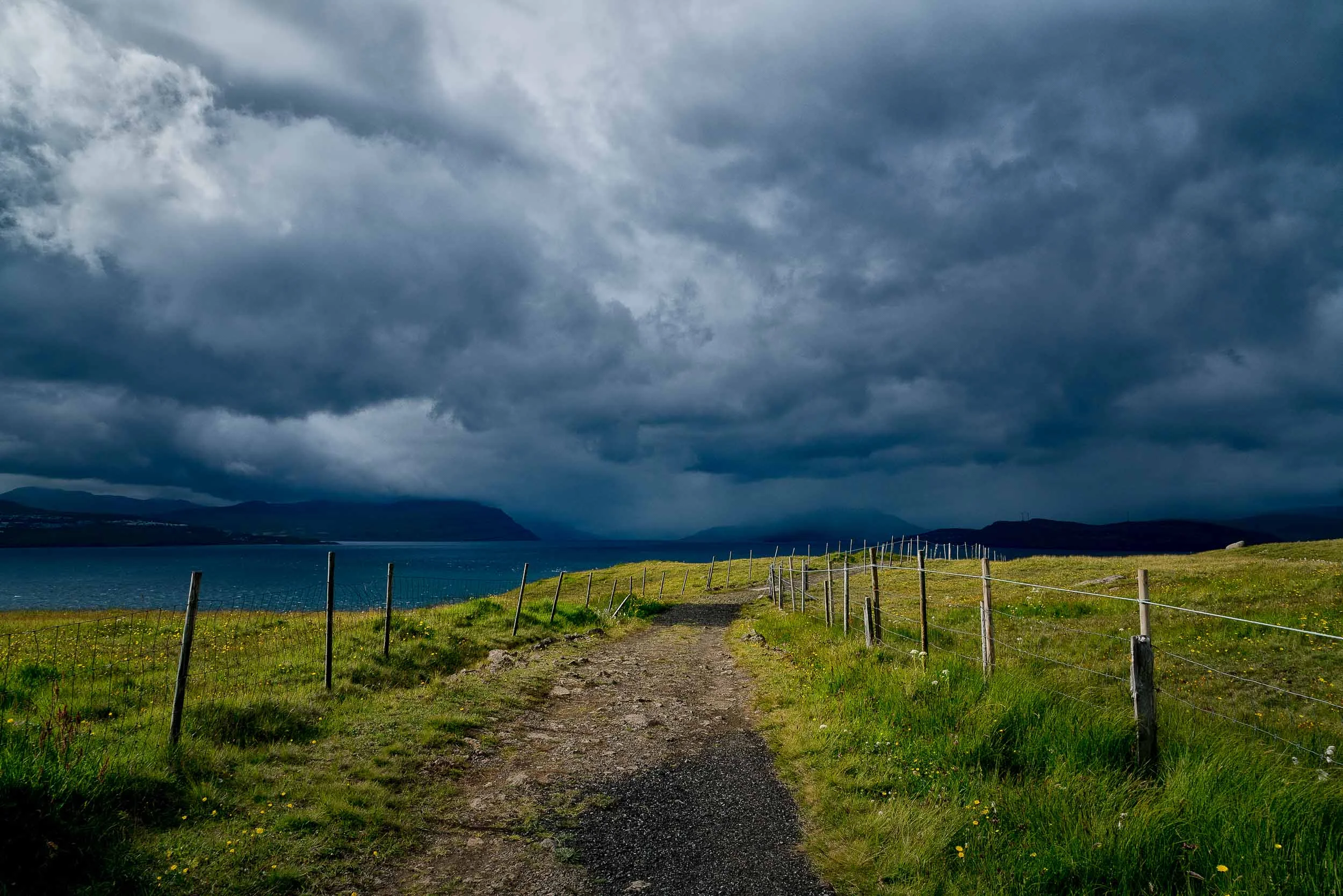 A path leads to the sea , under a stormy sky, at the edge of Nólsoy an island 4 km east of the Capital, Tórshavn in the Faroe Islands .