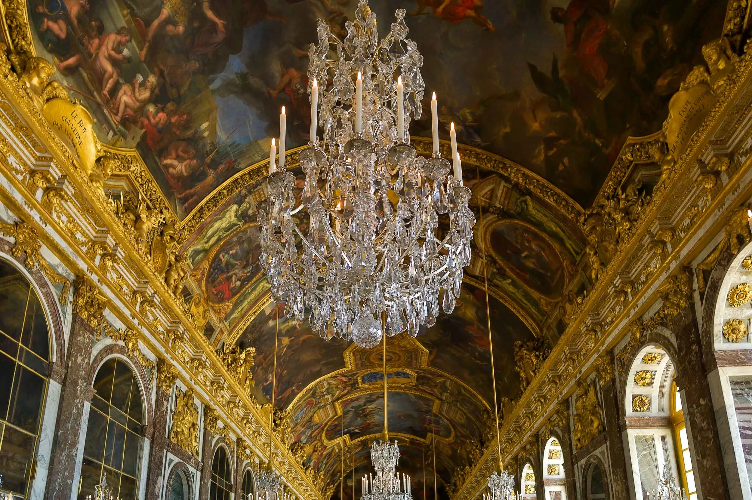 Magnificent chandelier and ornate ceiling murals at the Palace of Versailles, France.