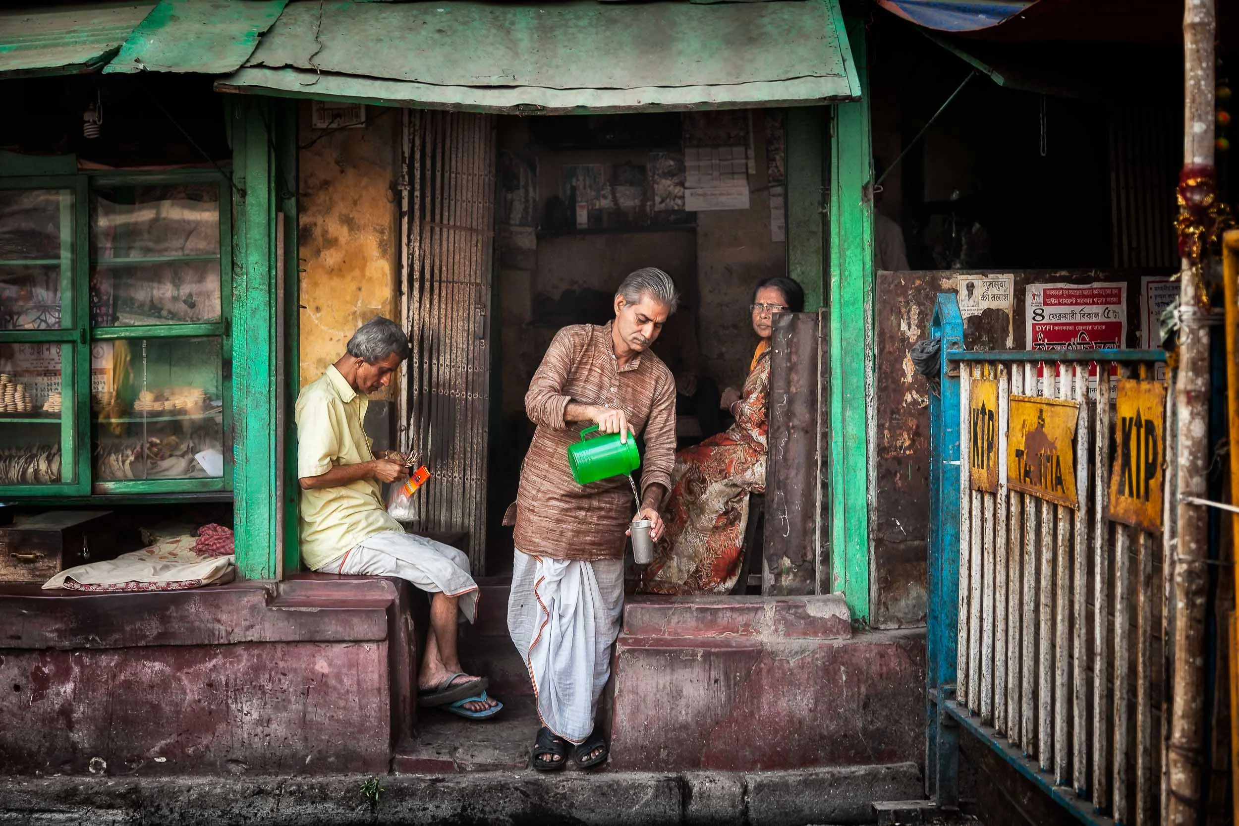A candid image of a cafe proprietor pouring a cup of water from a green jug in front of his establishment in Kolkata, India .