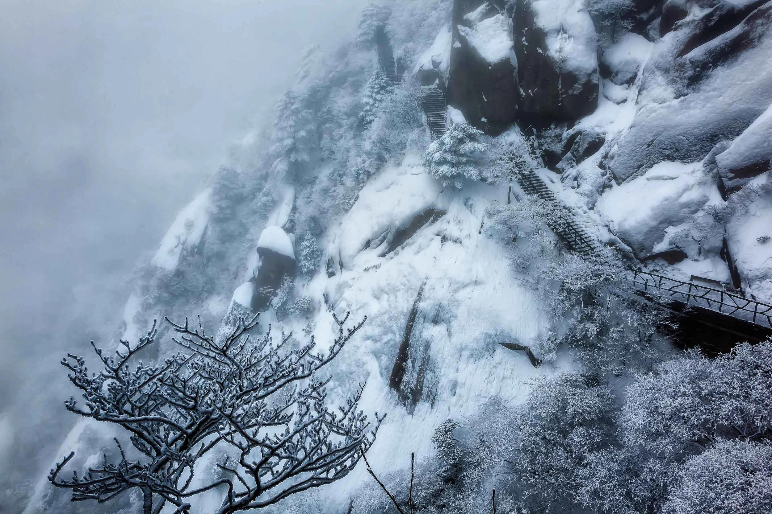 Dramatic landscape photo showing blue light and encroaching mist on Mount Huangshan.