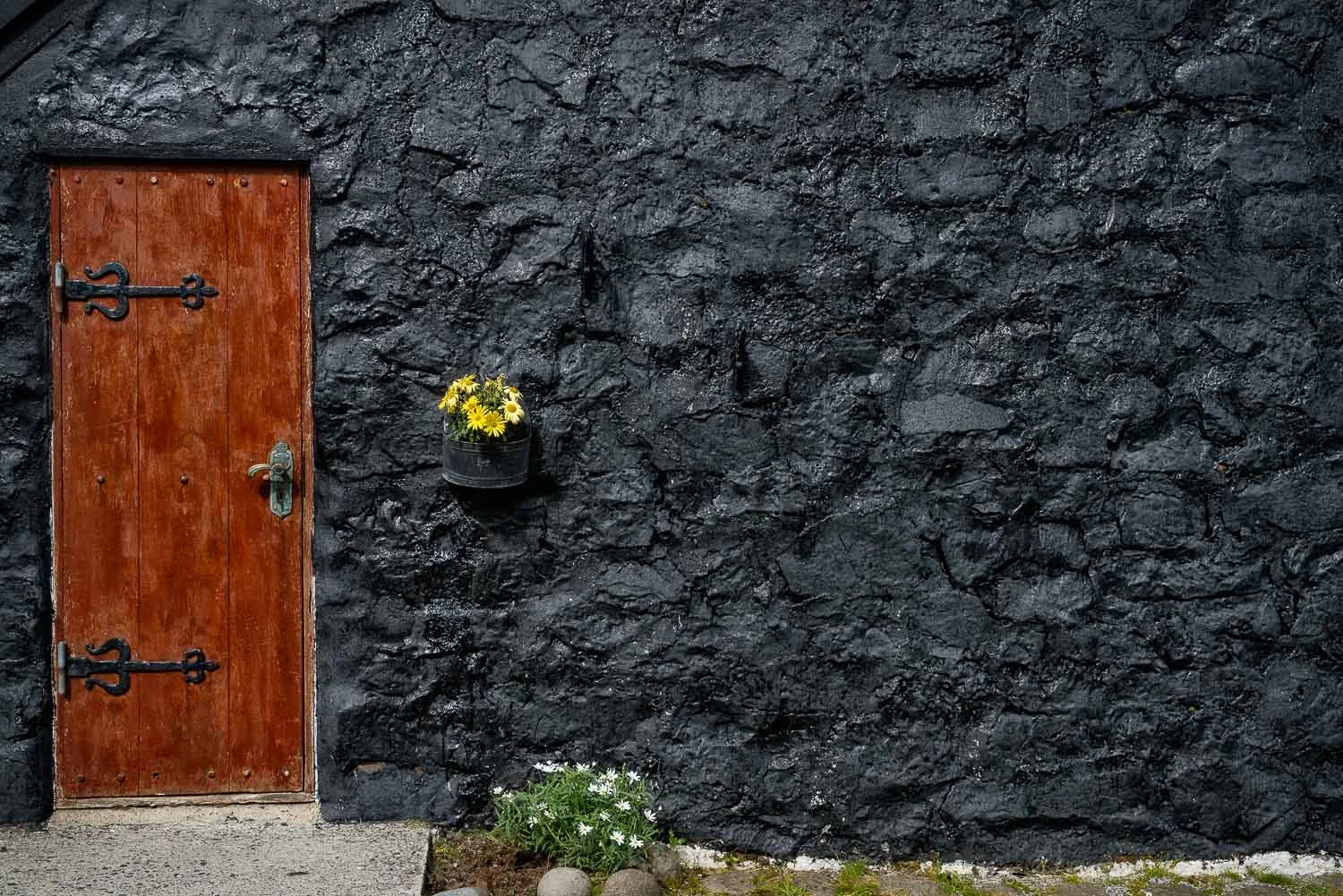 The front door and black tar wall of a traditional turf roof house in the Faroe Islands .